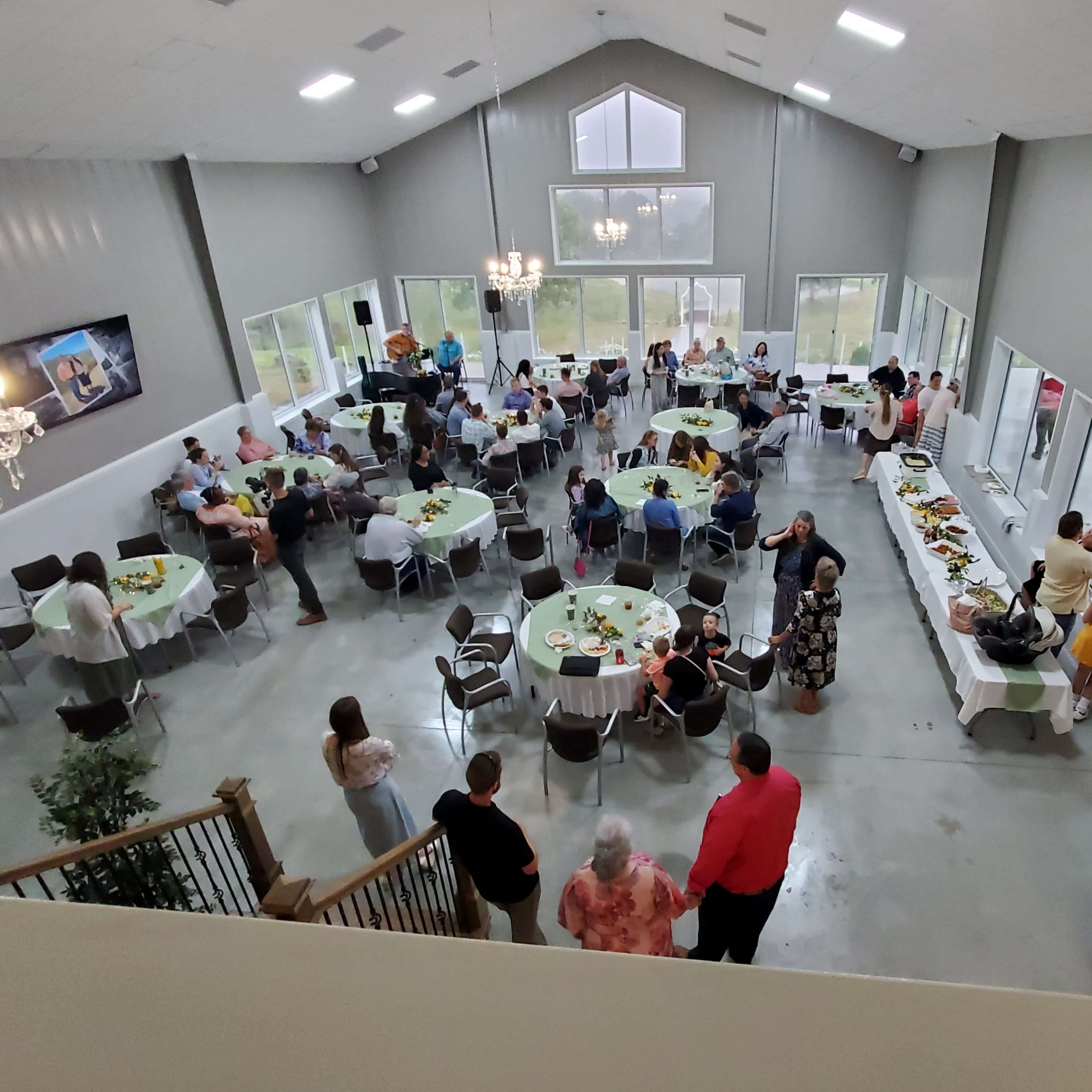A gathering is taking place in a spacious indoor venue with tables set for dining and guests mingling around a buffet.