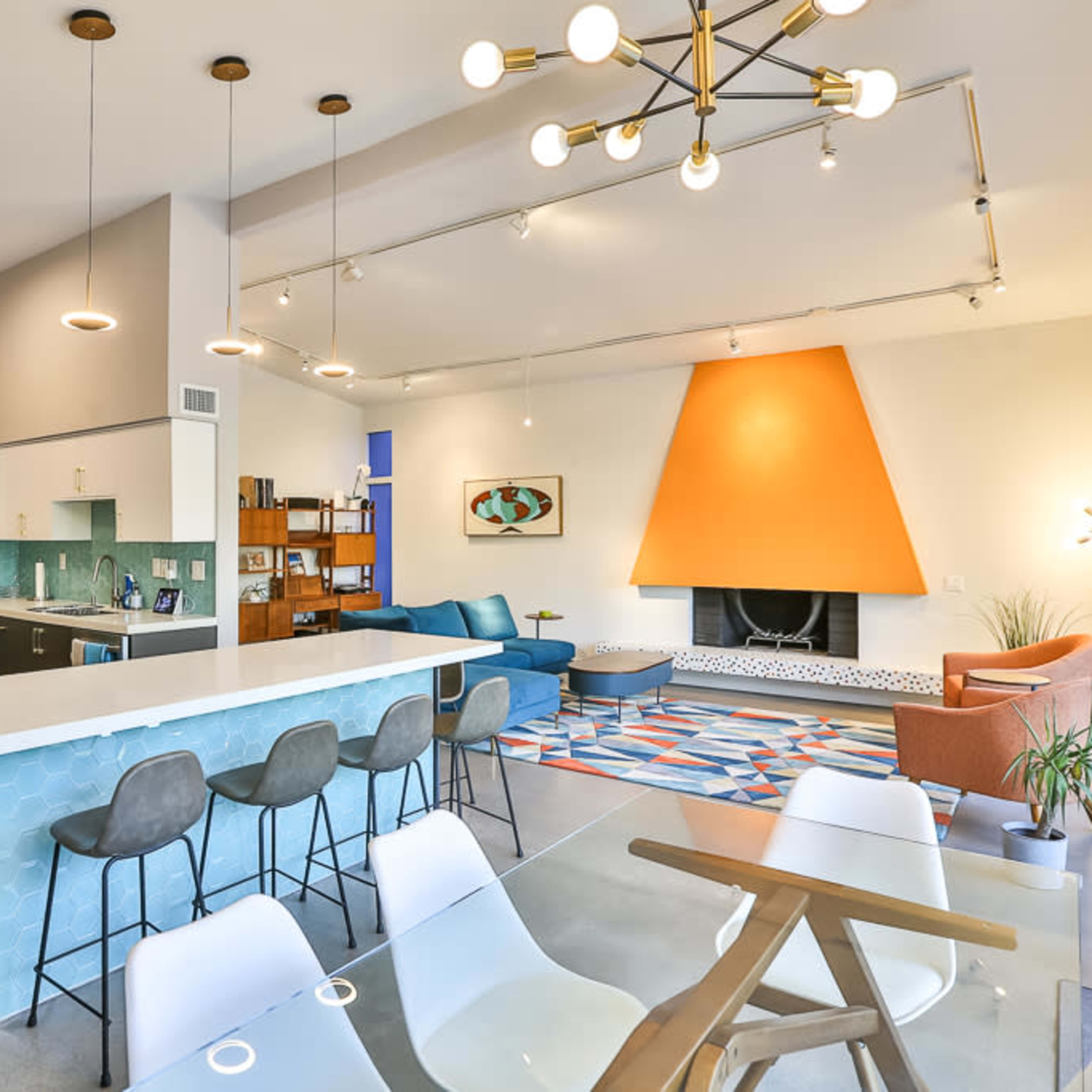 A modern open-concept living space featuring a kitchen, dining area, and living room with a vibrant orange fireplace as the focal point.