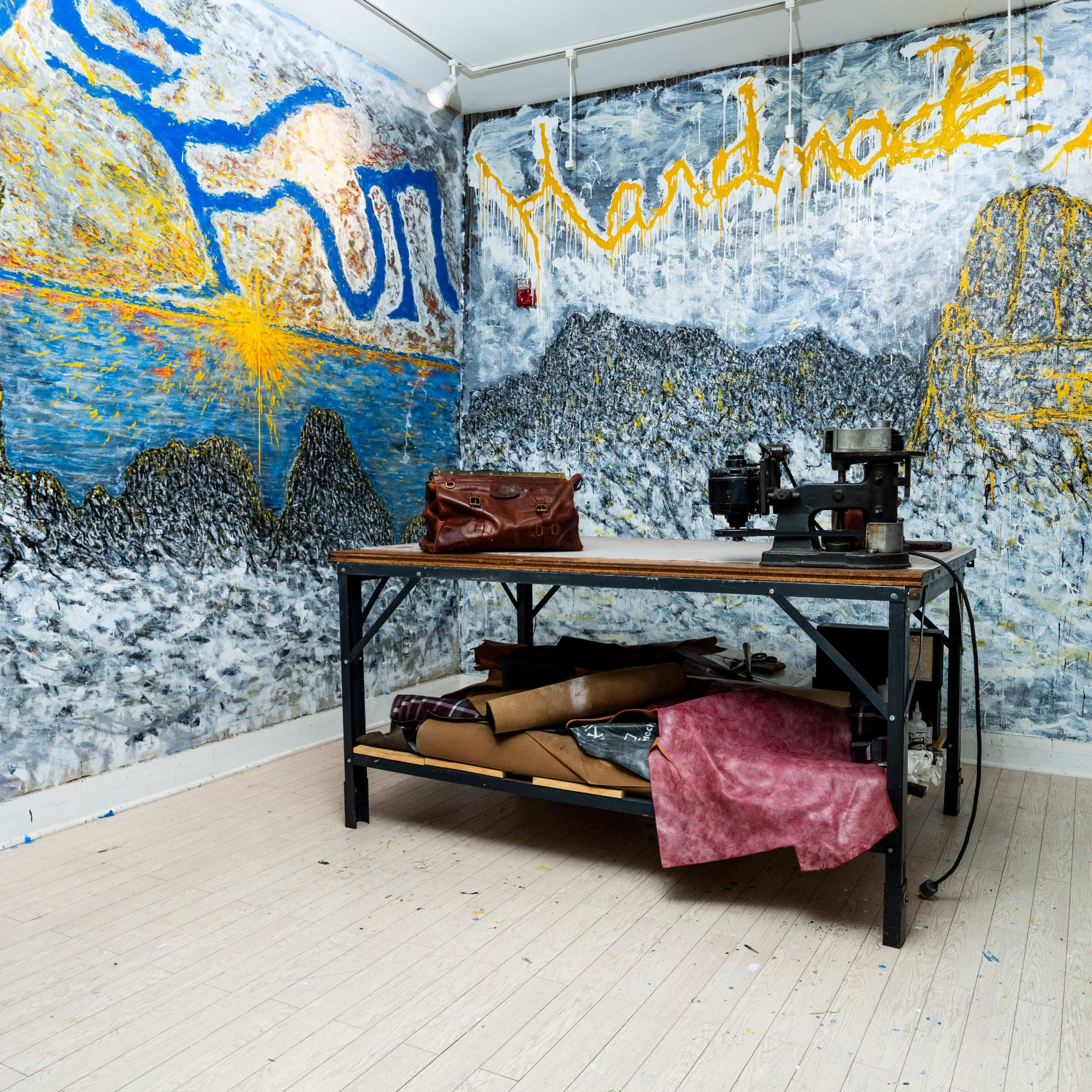 An interior room with abstract murals on the walls, a table with a sewing machine, and assorted materials stacked underneath.