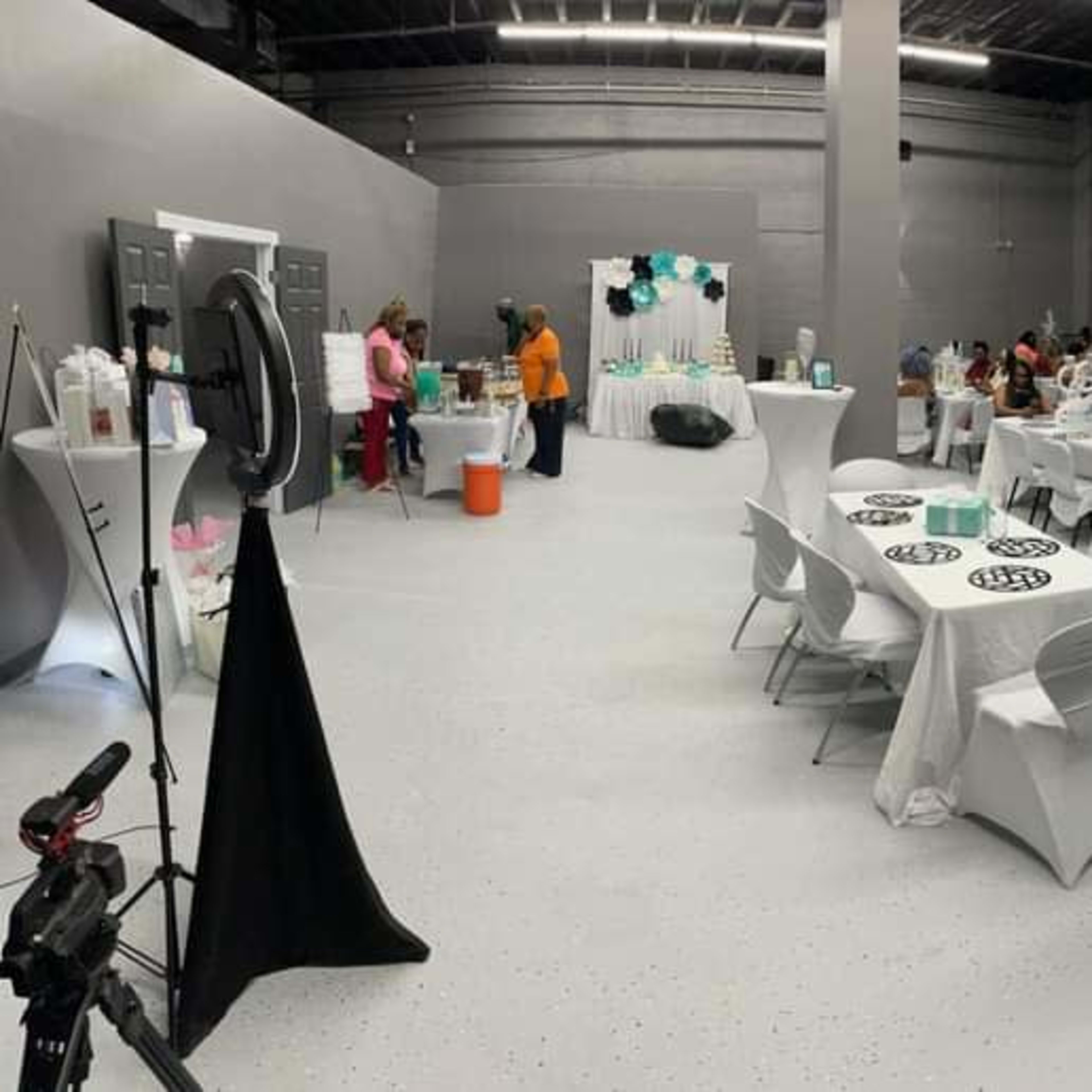 An indoor event space with neatly arranged tables, decorations in teal and white, and guests seated throughout the area.