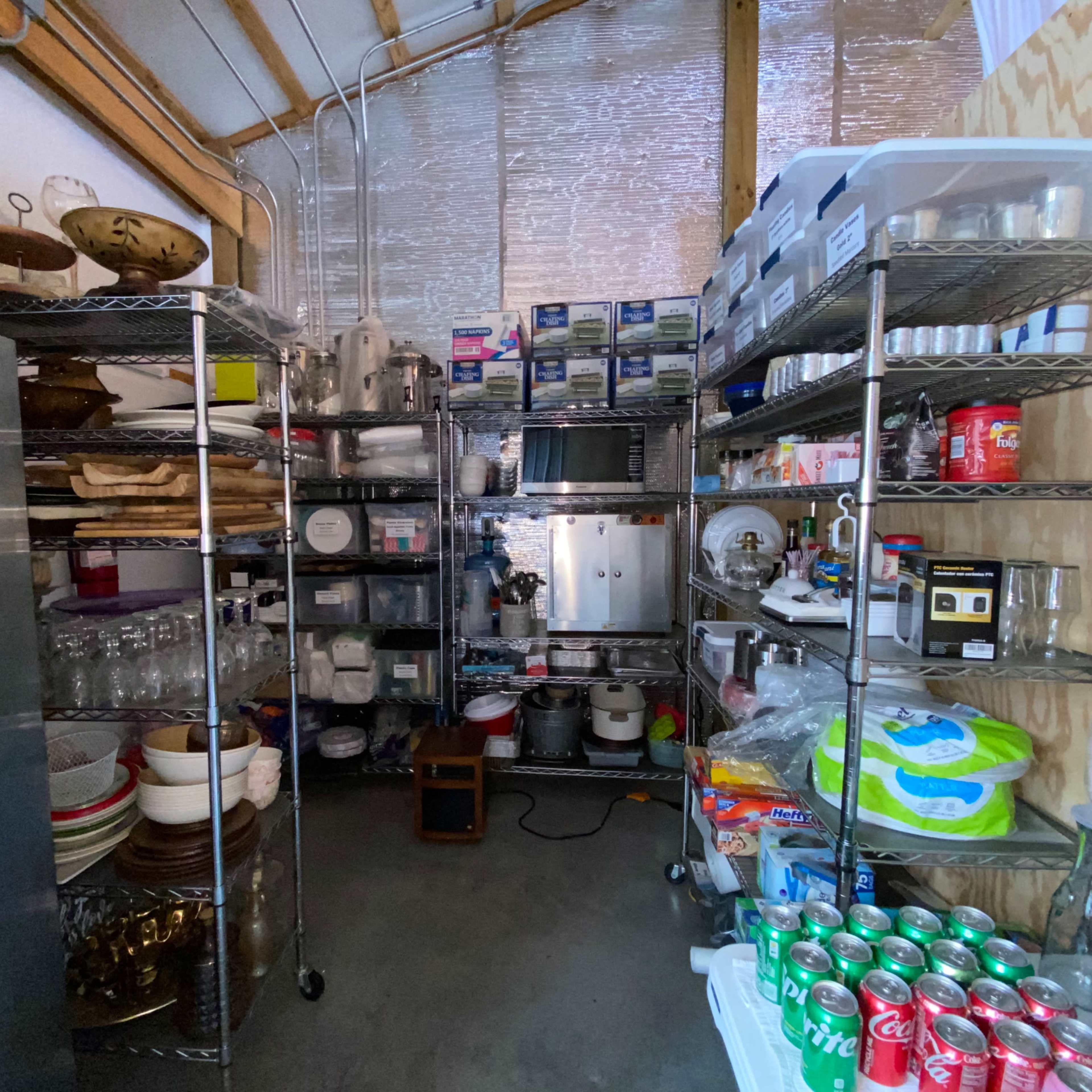 A storage area features metal shelves filled with kitchenware, containers, and a microwave, with various food and beverage items organized on the floor.