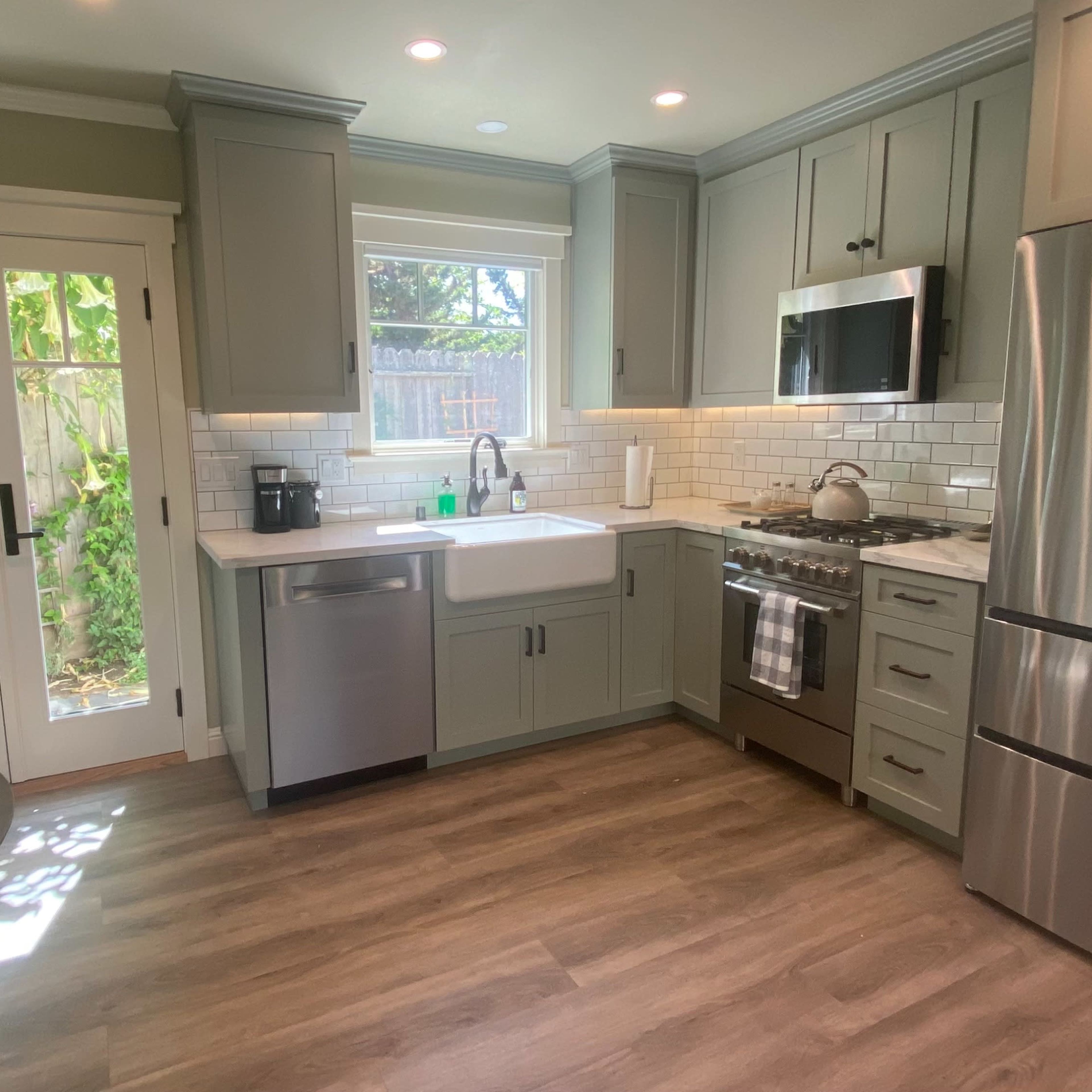 A modern kitchen with gray cabinets, stainless steel appliances, a white farmhouse sink, and a small dining table.