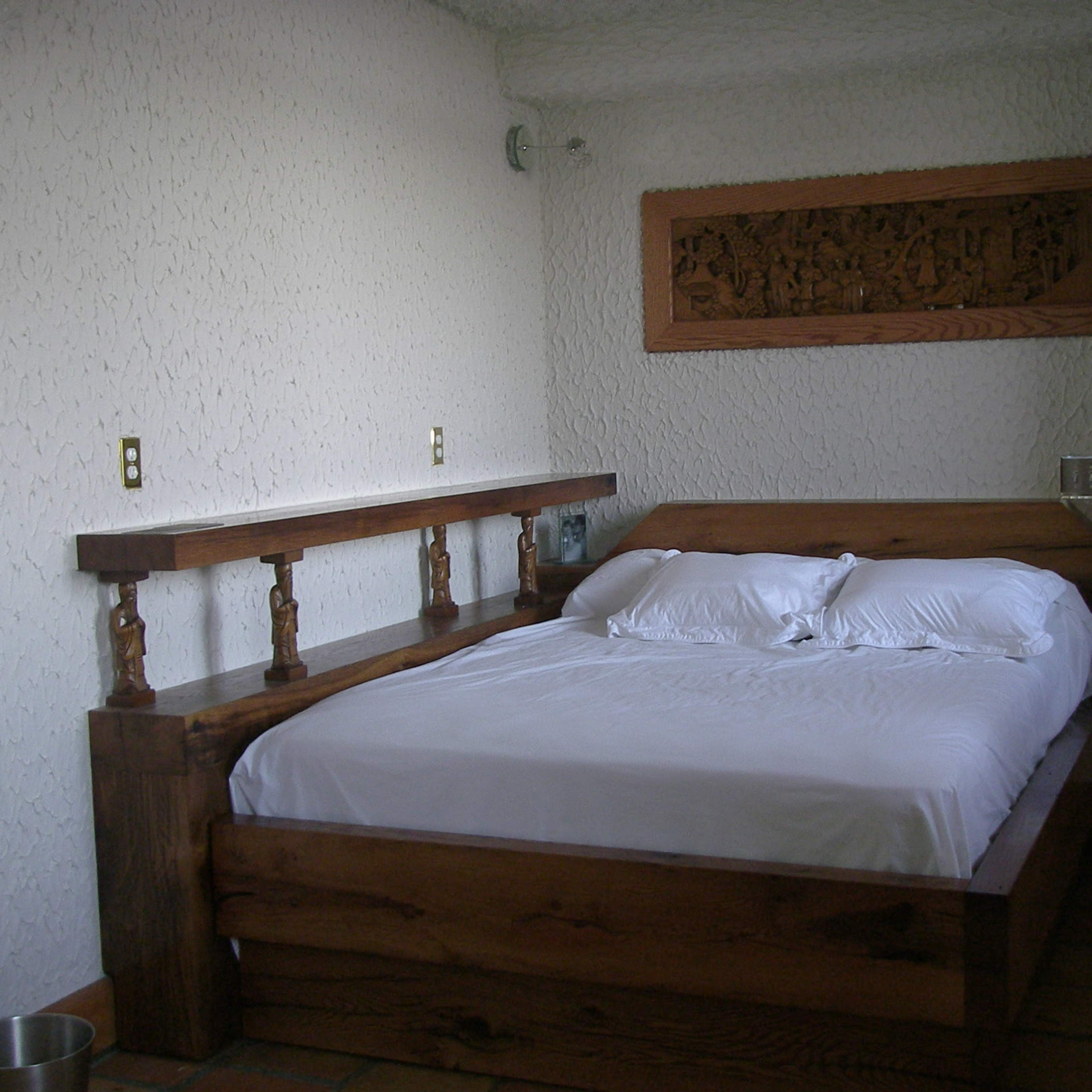 A simple bedroom with a wooden bed frame, a white bedspread, and textured walls.