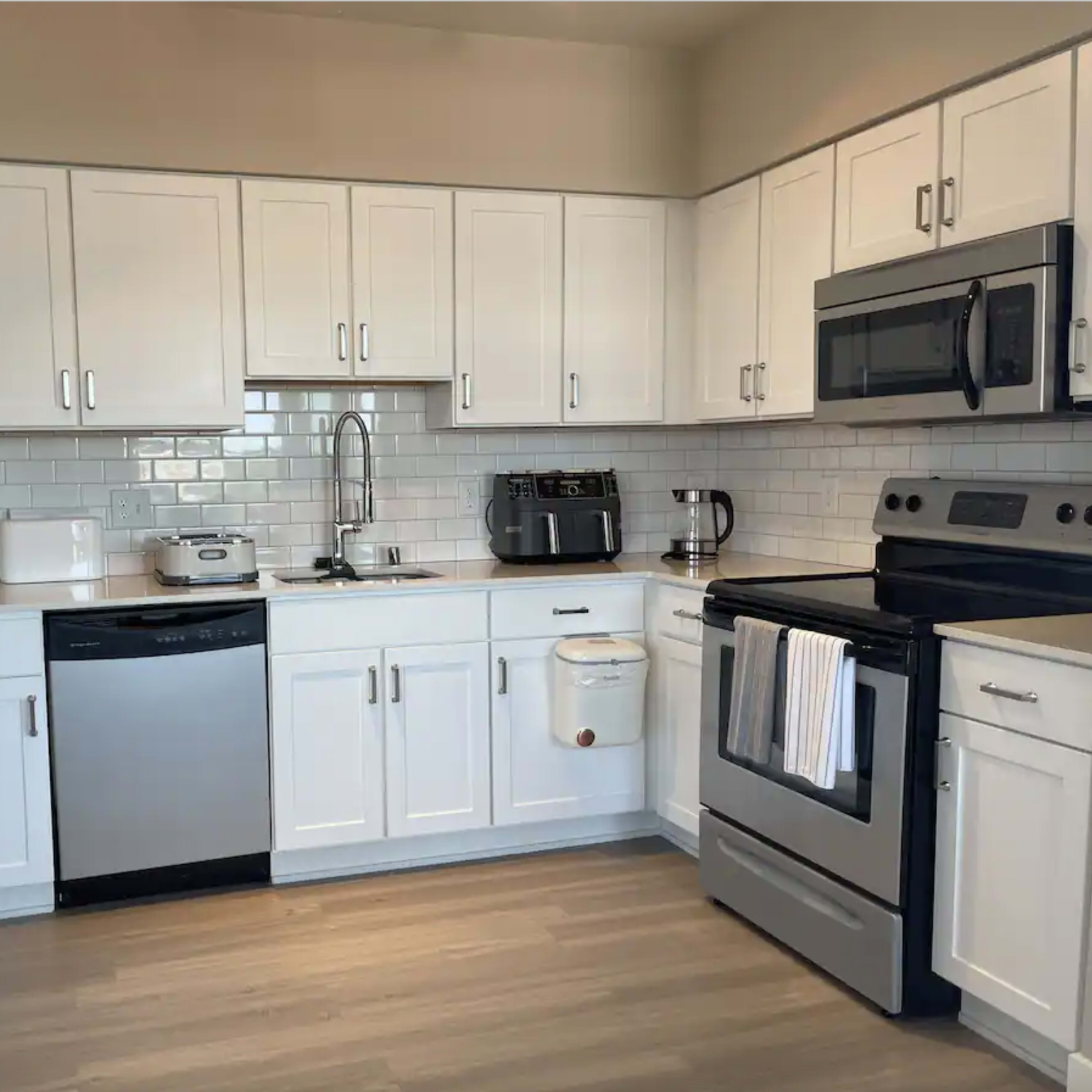 A modern kitchen features white cabinetry, stainless steel appliances, and a light-colored countertop.