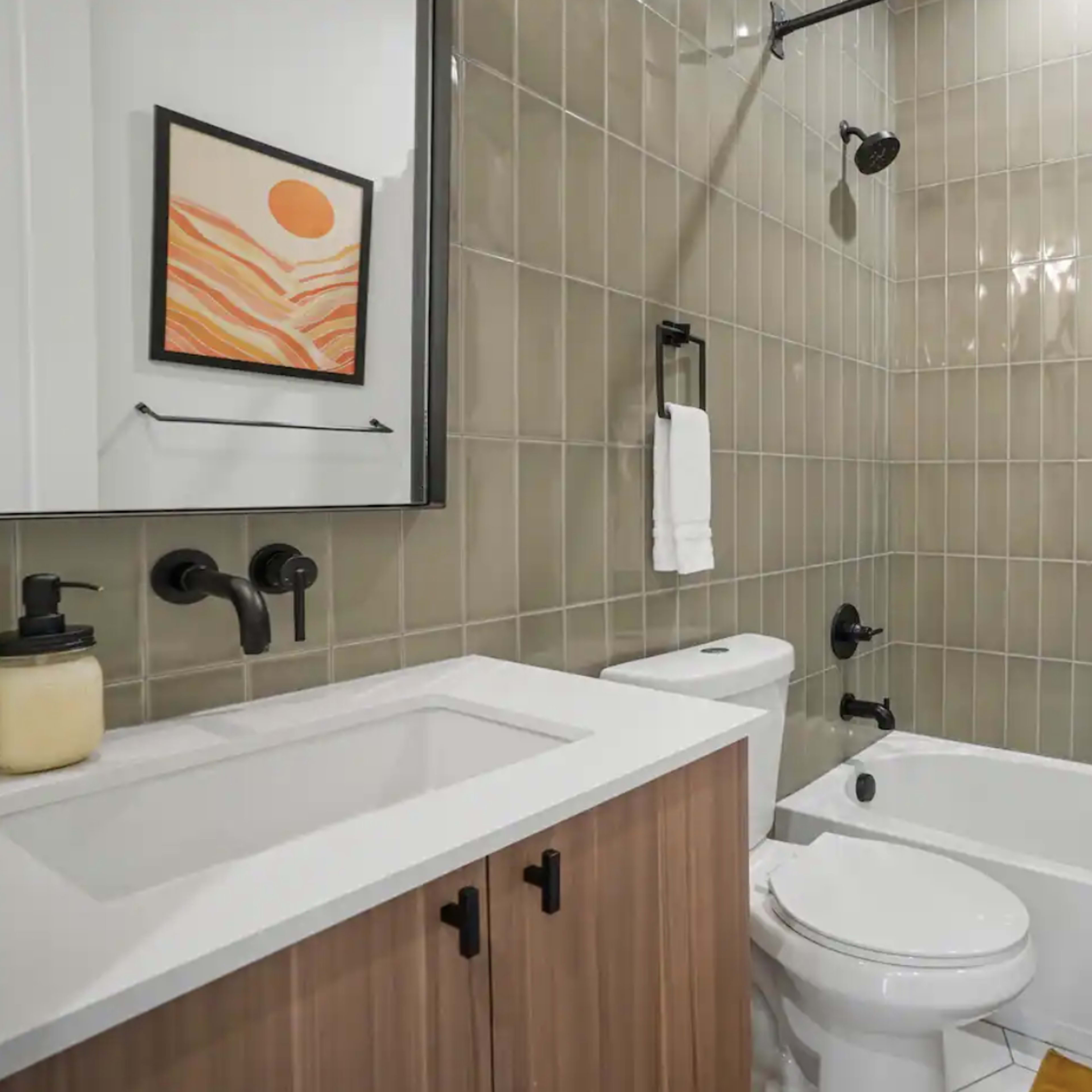 A bathroom with a shower-bathtub combination, a toilet, a sink with a wooden cabinet, and modern fixtures on the walls.