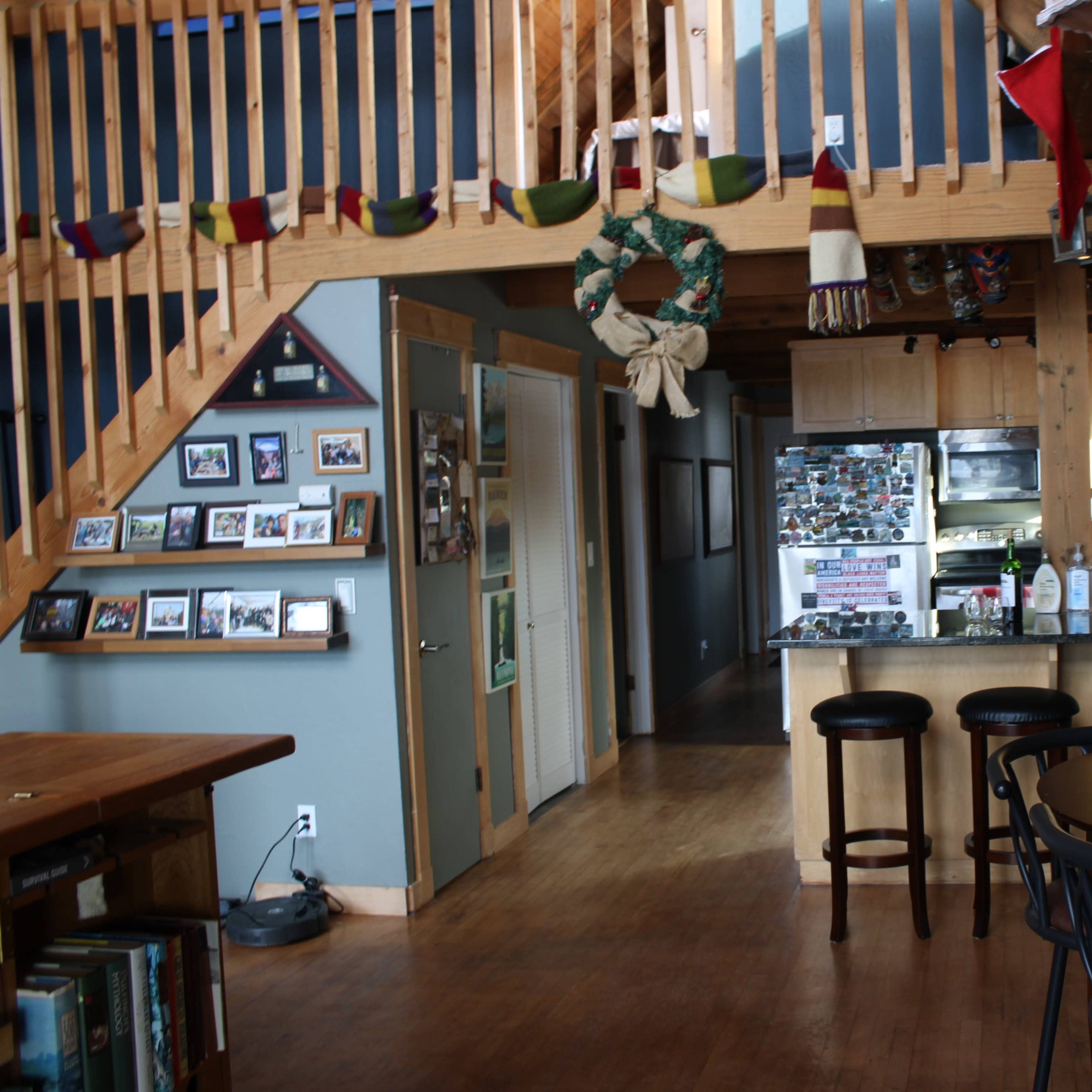 A wooden interior of a loft-style living space with a kitchen, dining area, and a staircase leading to an upper level.