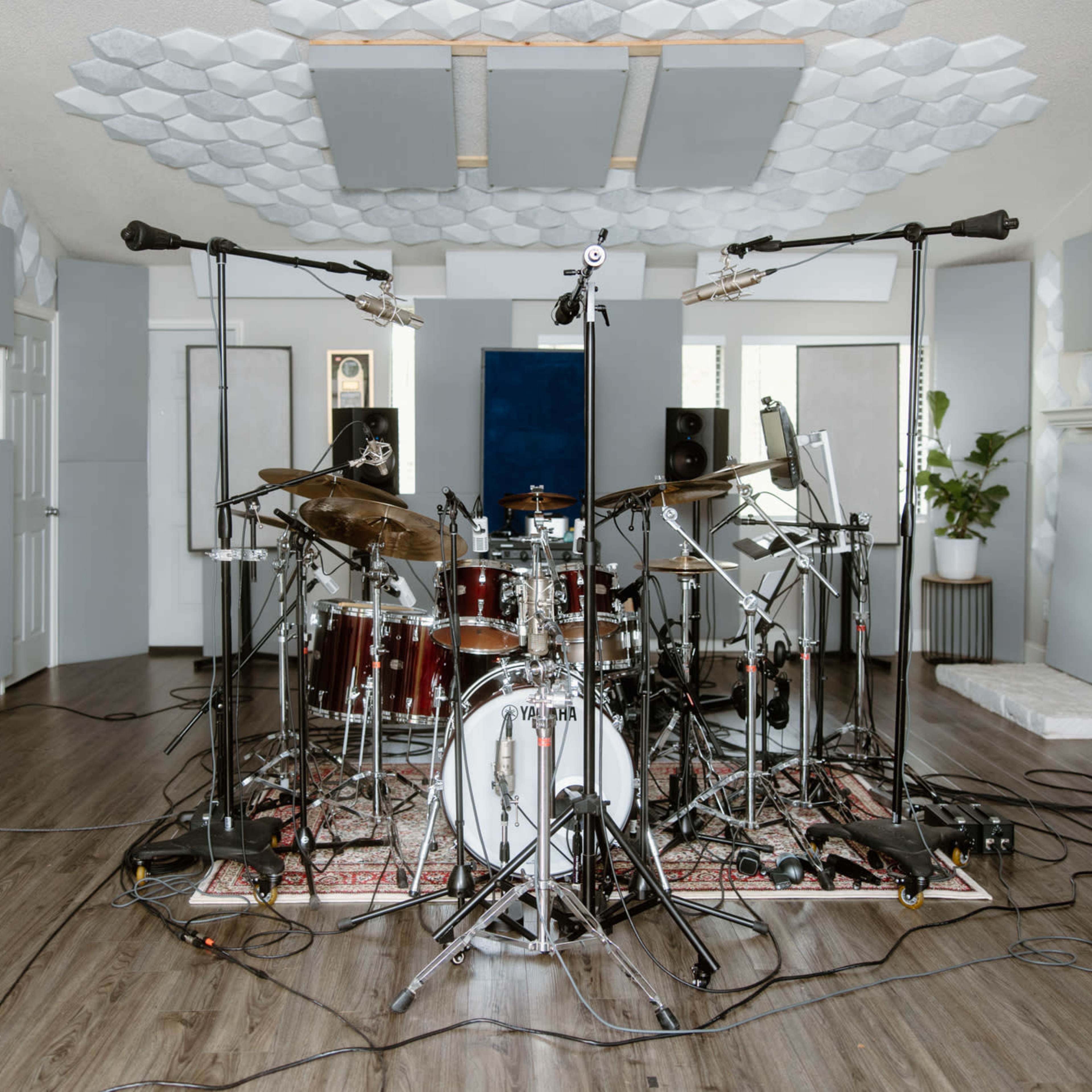 A recording studio with a drum set surrounded by soundproof panels and microphone stands on a wooden floor.
