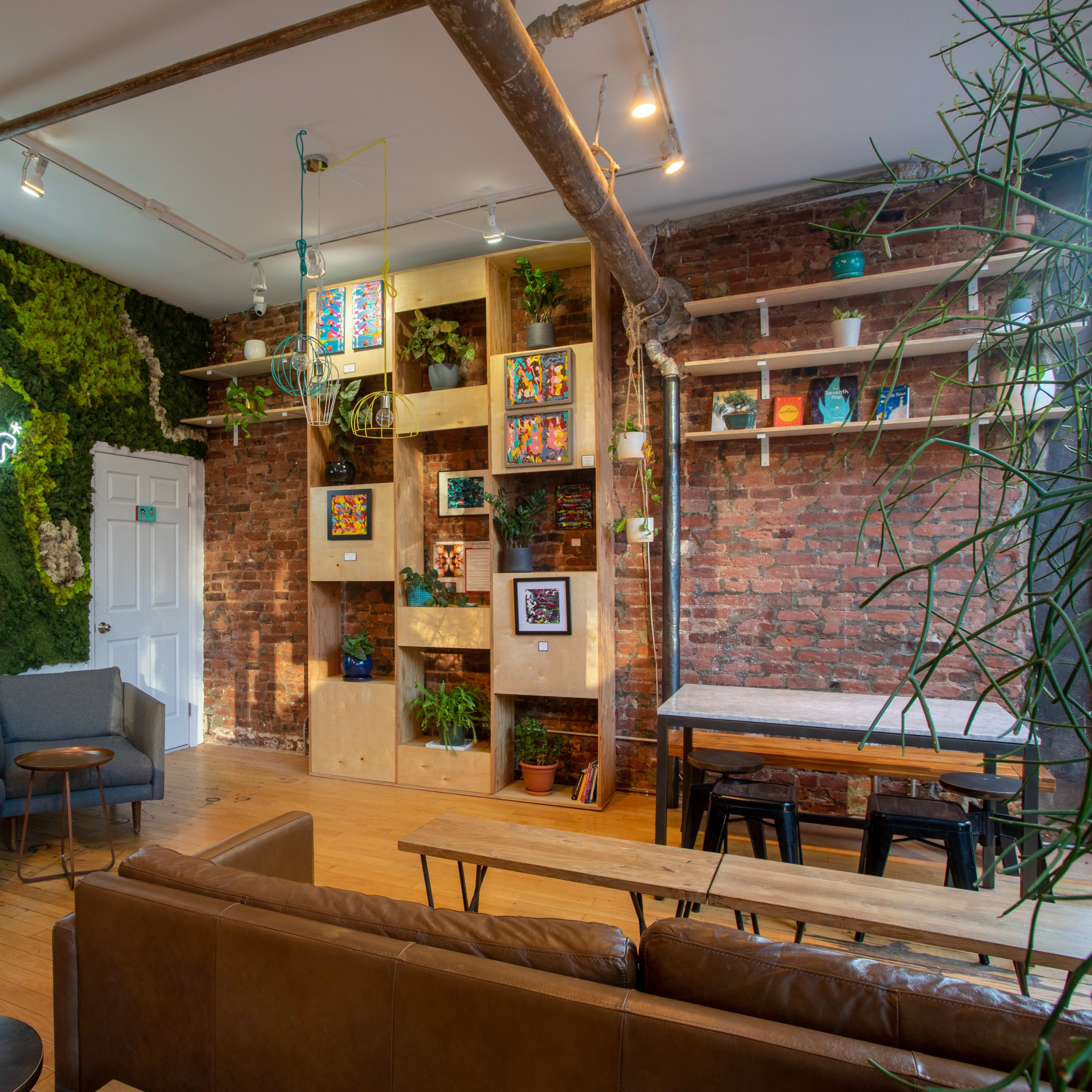 A stylish indoor space featuring a green moss wall, brick accents, wooden furniture, and various plants on shelves.