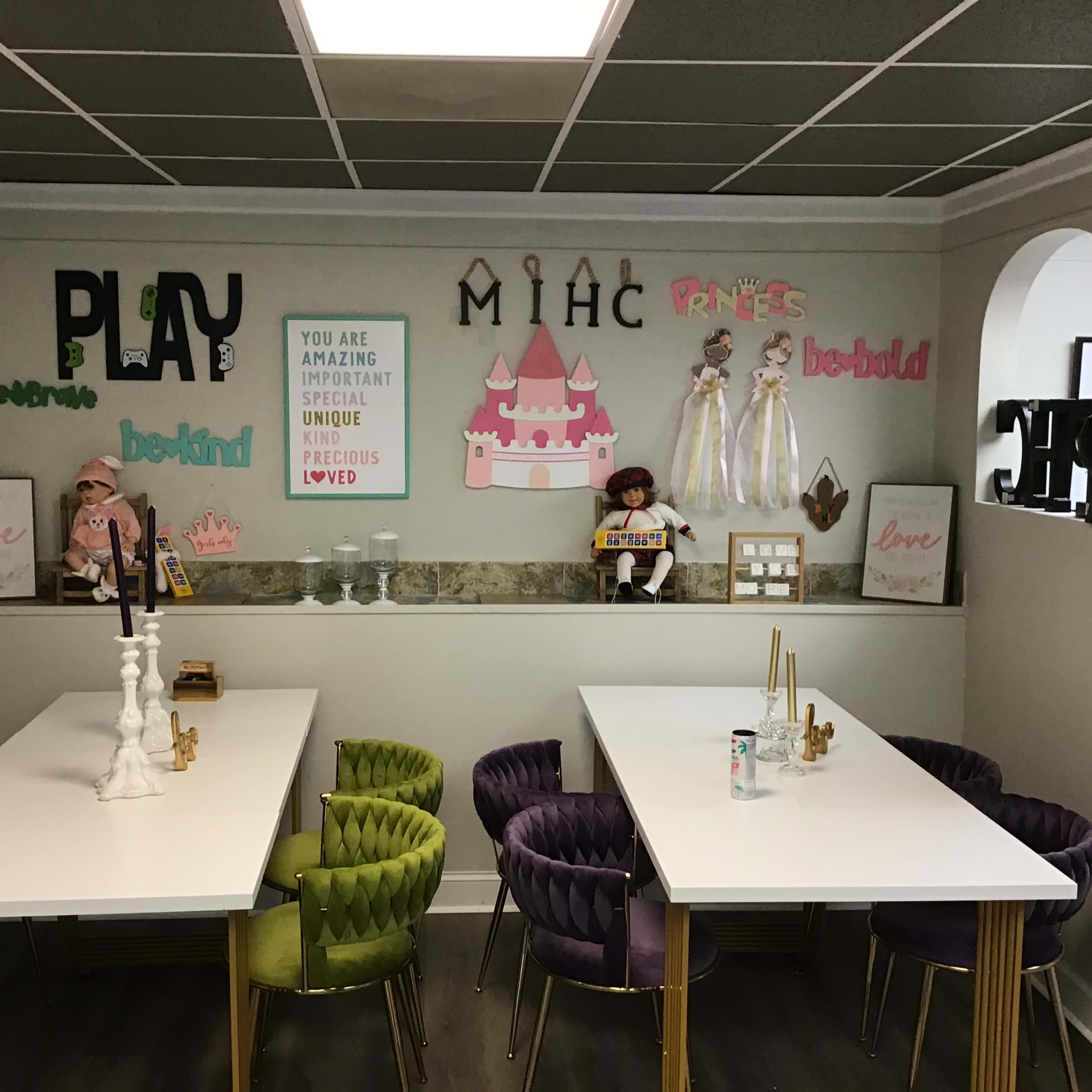 A brightly decorated room with two white tables, colorful chairs, and a wall adorned with playful signs and decorative items related to children's themes.