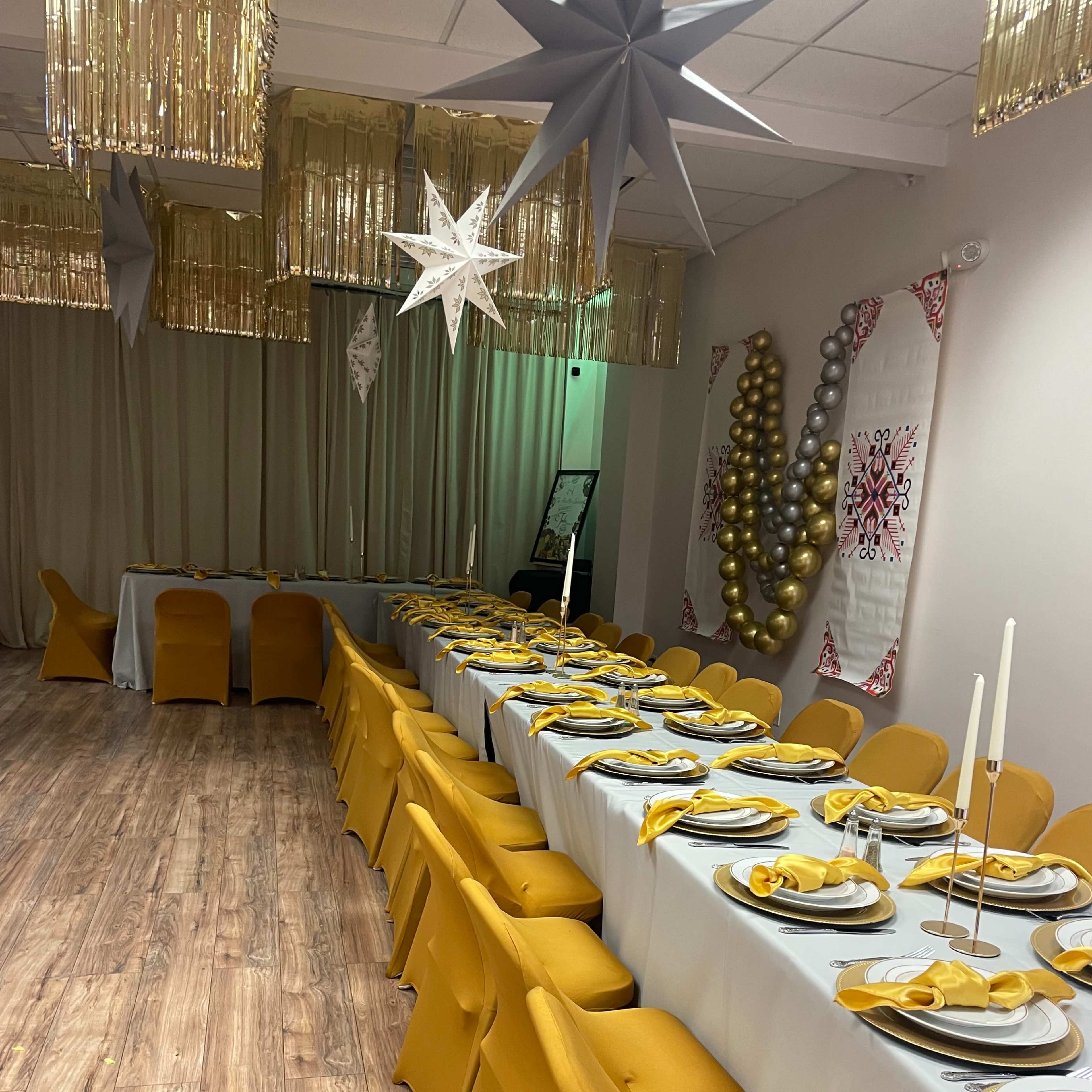 A long dining table set with yellow napkins and tableware, surrounded by golden decorations and featuring a festive atmosphere.
