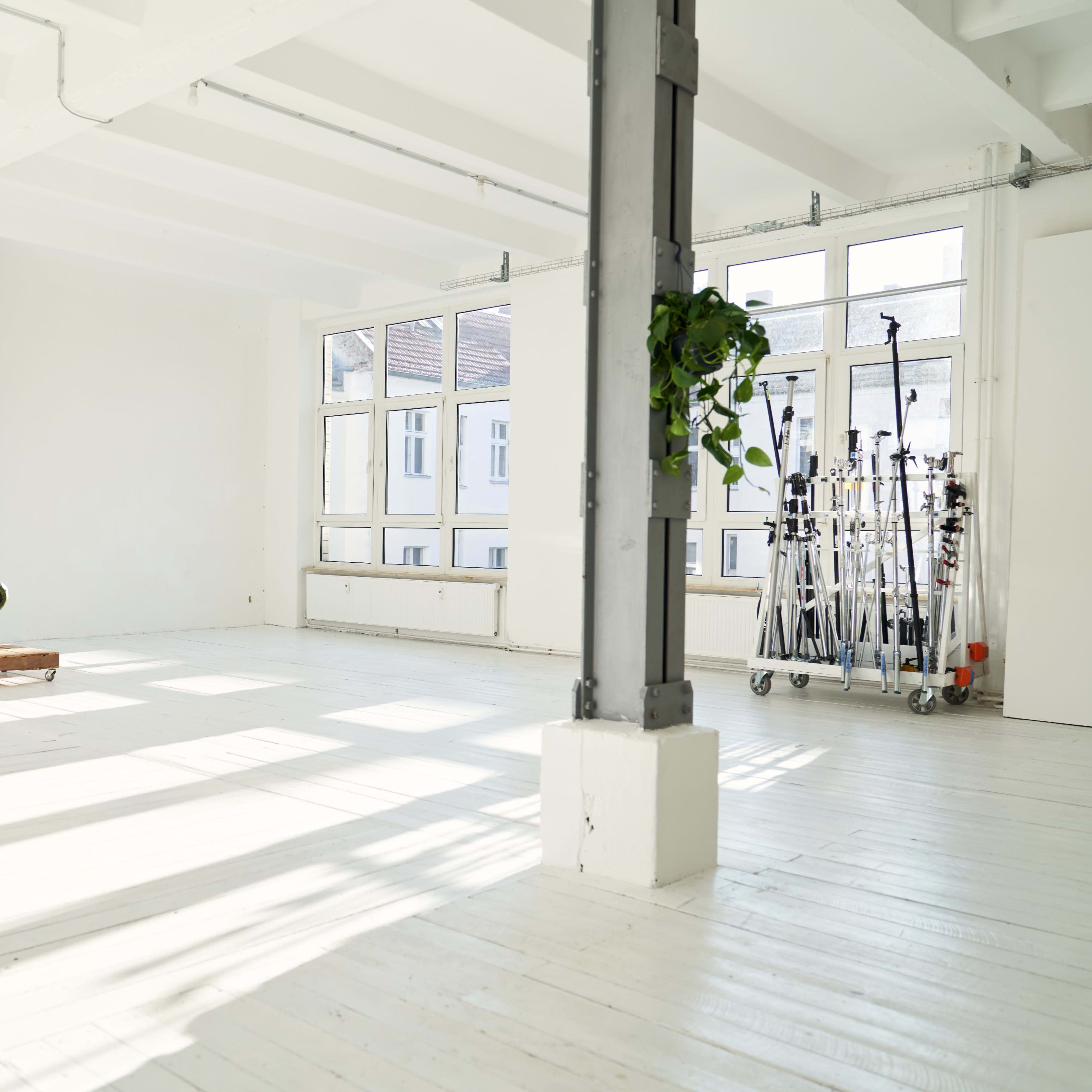 A bright, spacious room with a green couch, a wooden coffee table, and lighting equipment on a cart near the windows.