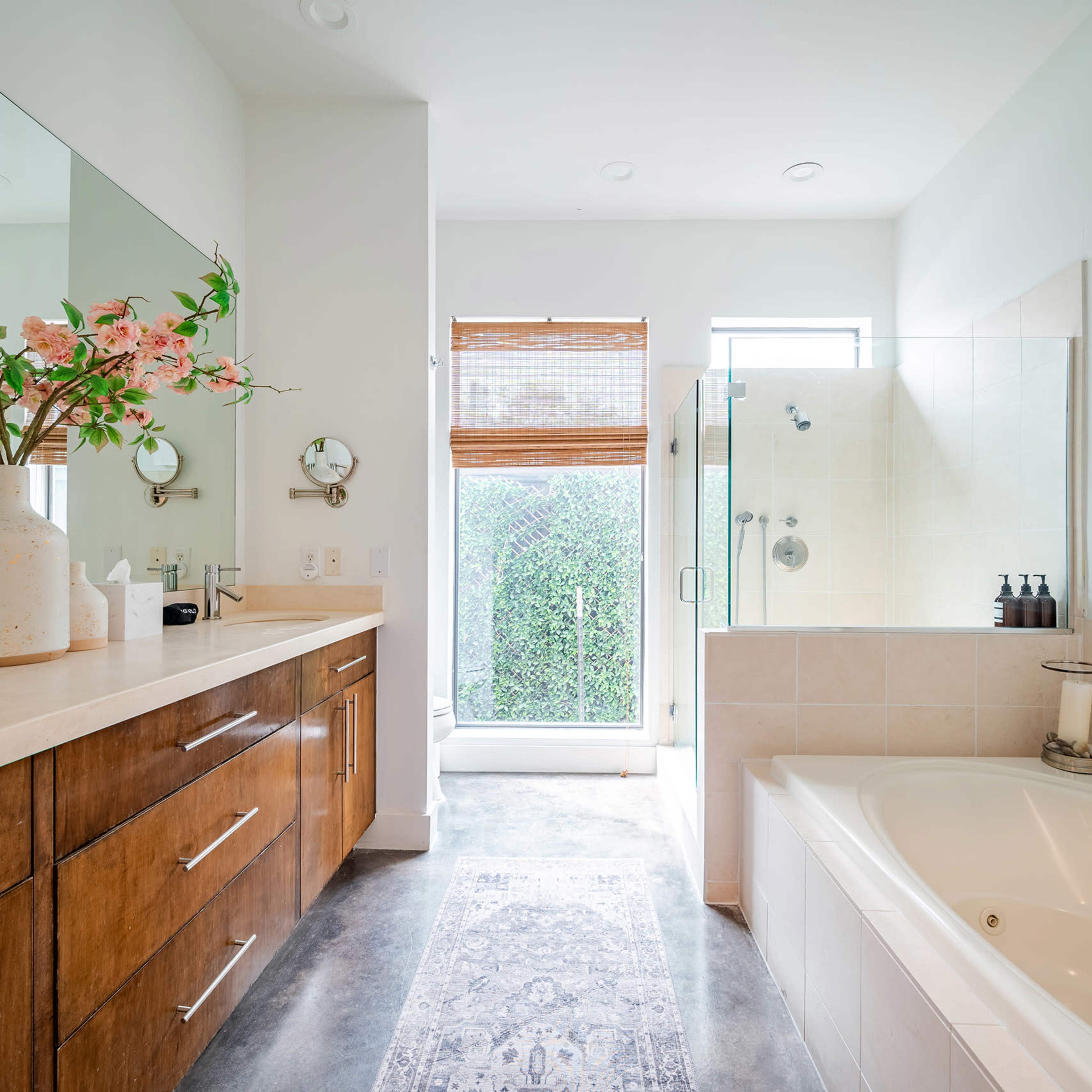 A modern bathroom features a large bathtub, double sinks, a glass shower, and plants by the window.