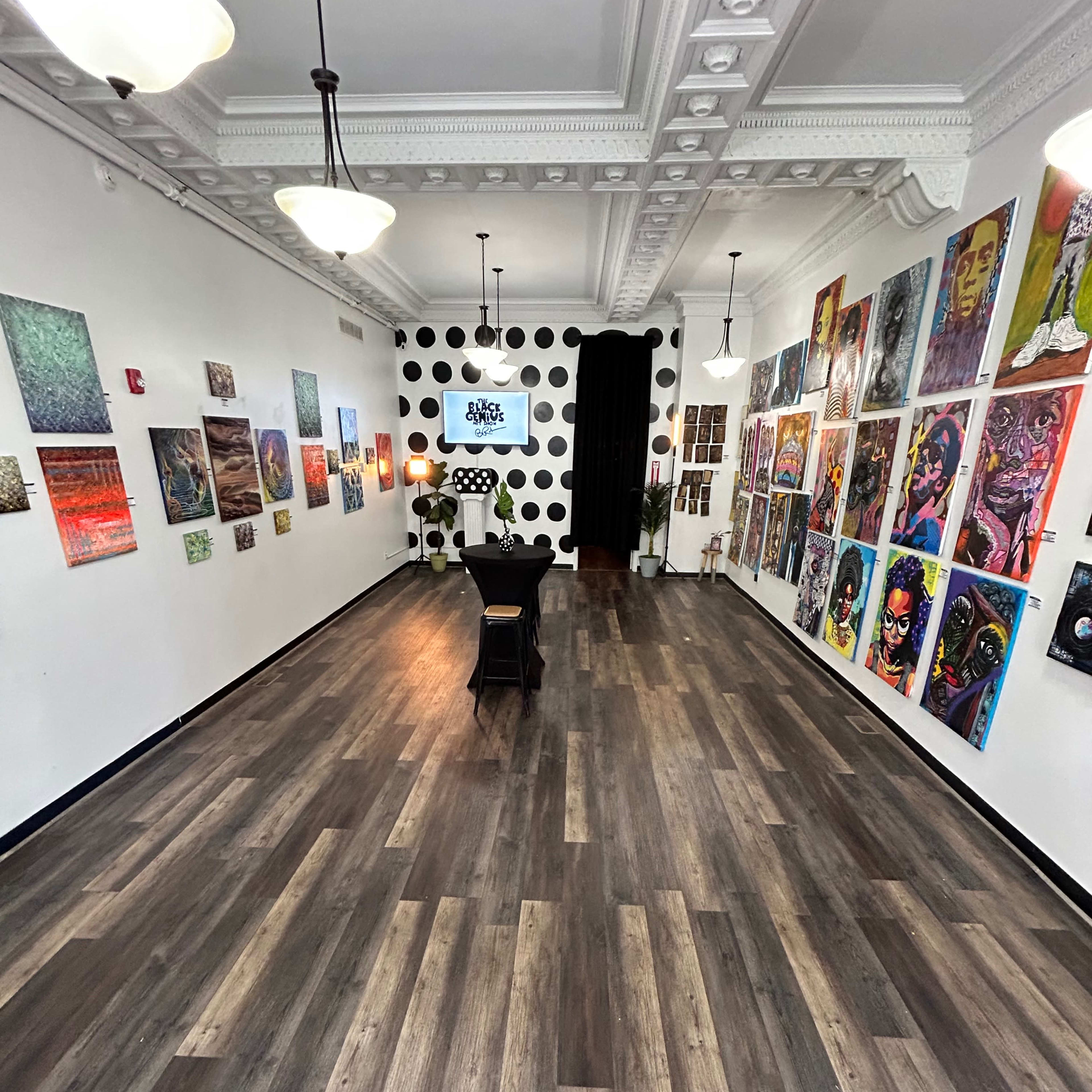 An art gallery with wooden flooring, displaying a variety of colorful artwork on the walls and featuring furniture in the center of the space.
