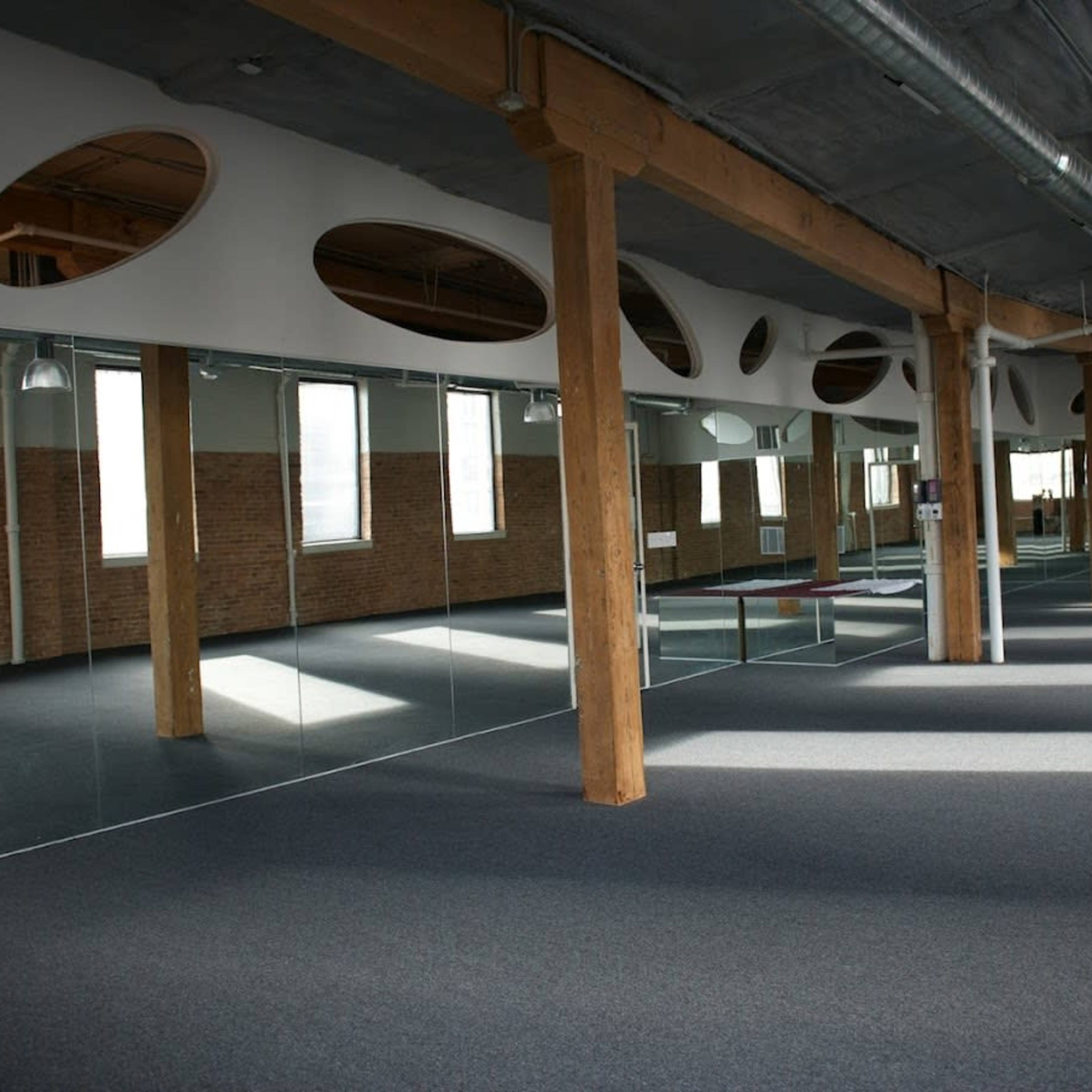A spacious studio with wooden beams, large mirrors on one side, and windows allowing natural light to enter.