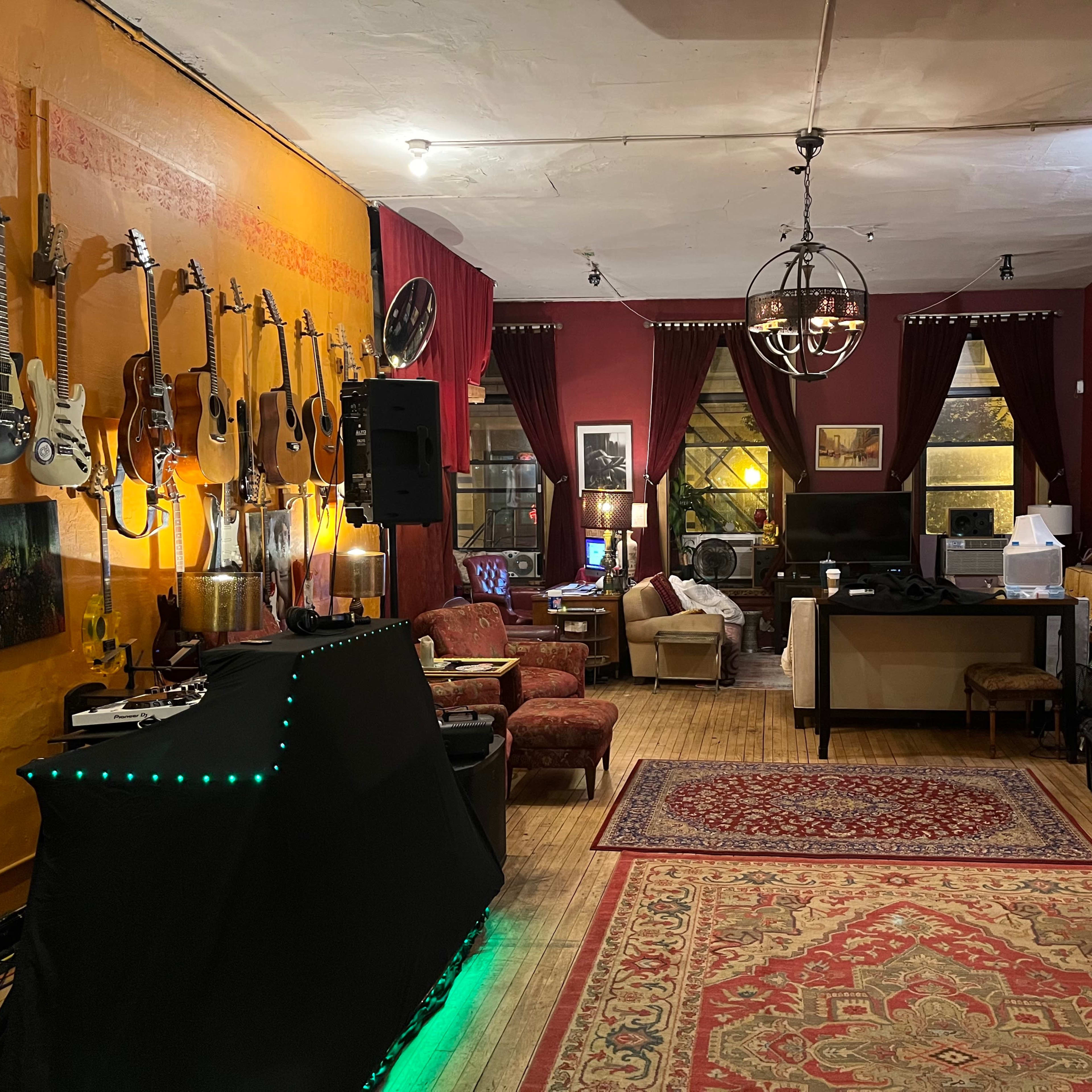 A cozy room with various guitars hanging on the wall, a sound system setup, and seating areas arranged around a central rug.