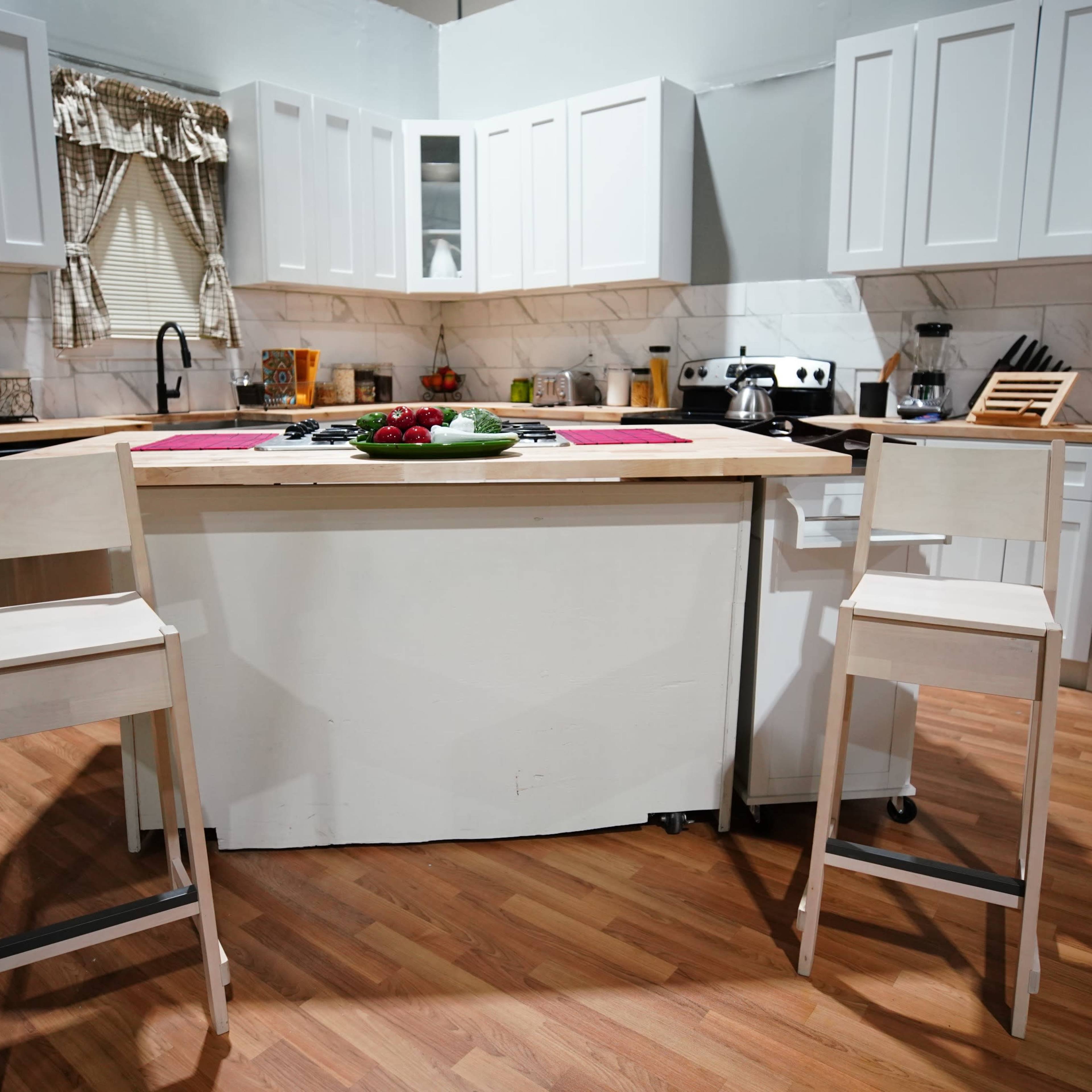 A modern kitchen features a central island with two high stools and a bowl of fruit on the countertop.