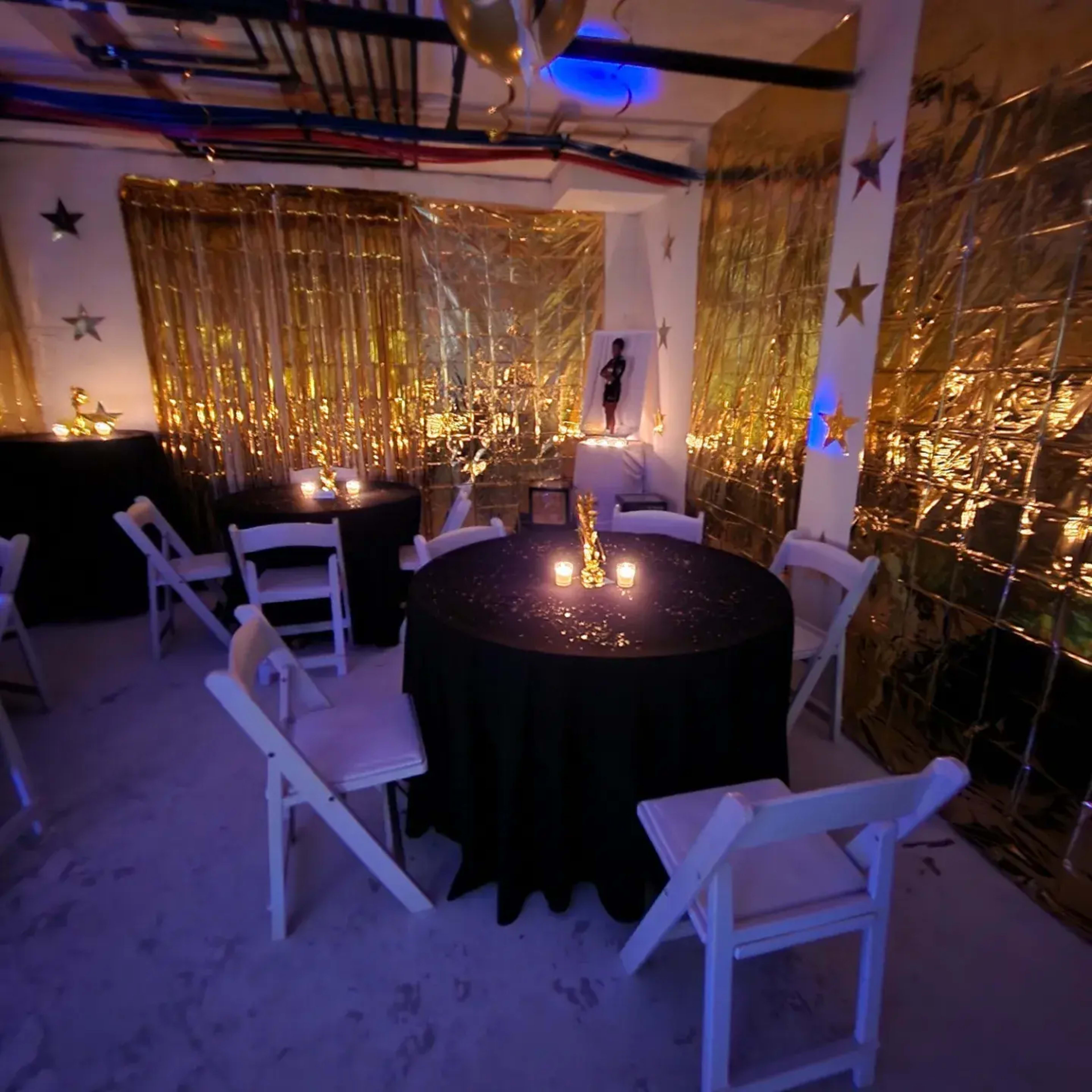 A decorated indoor space with tables covered in black cloth, golden drapery, and dim lighting from candles.