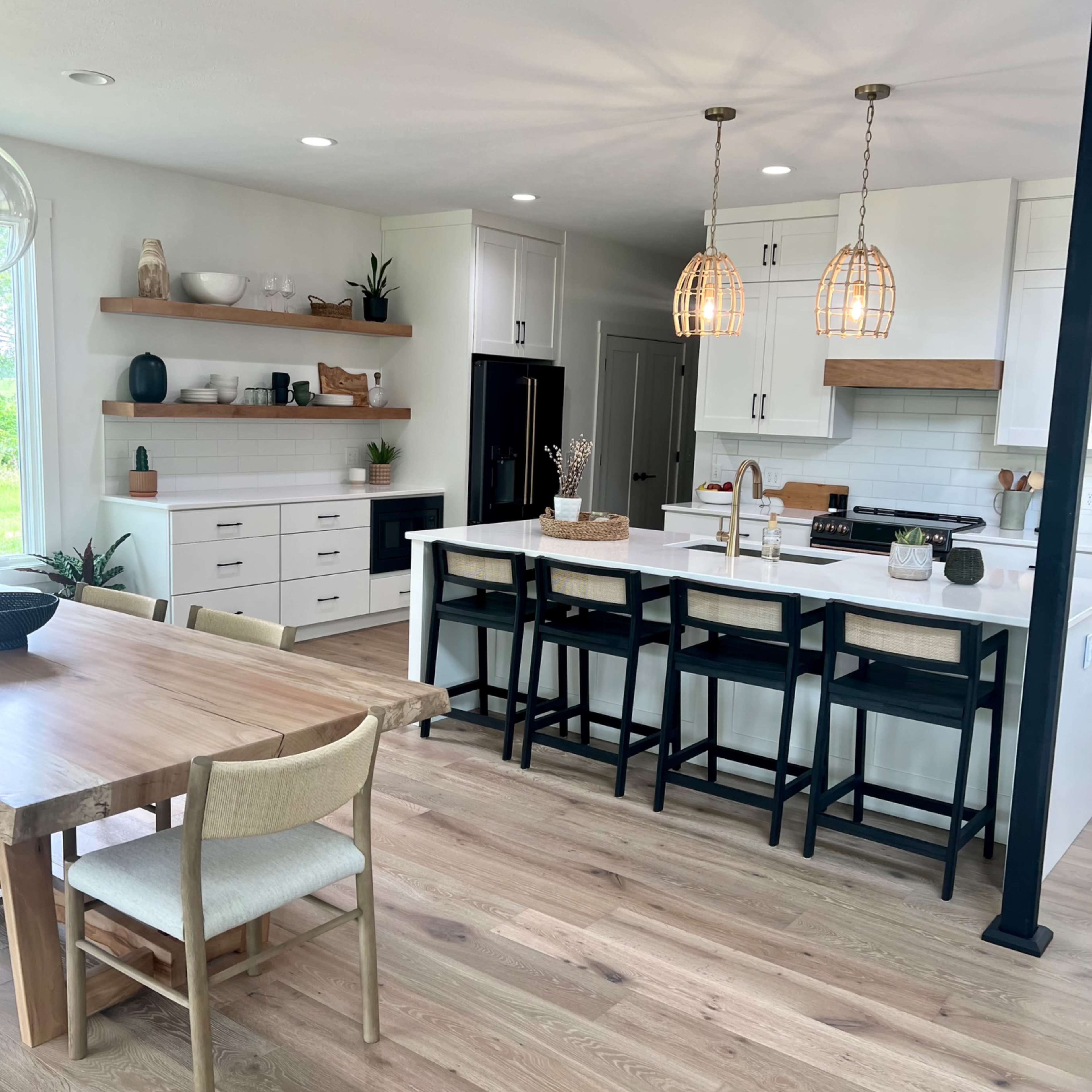 A modern kitchen featuring white cabinetry, a central island with bar seating, and a wooden dining table with chairs.