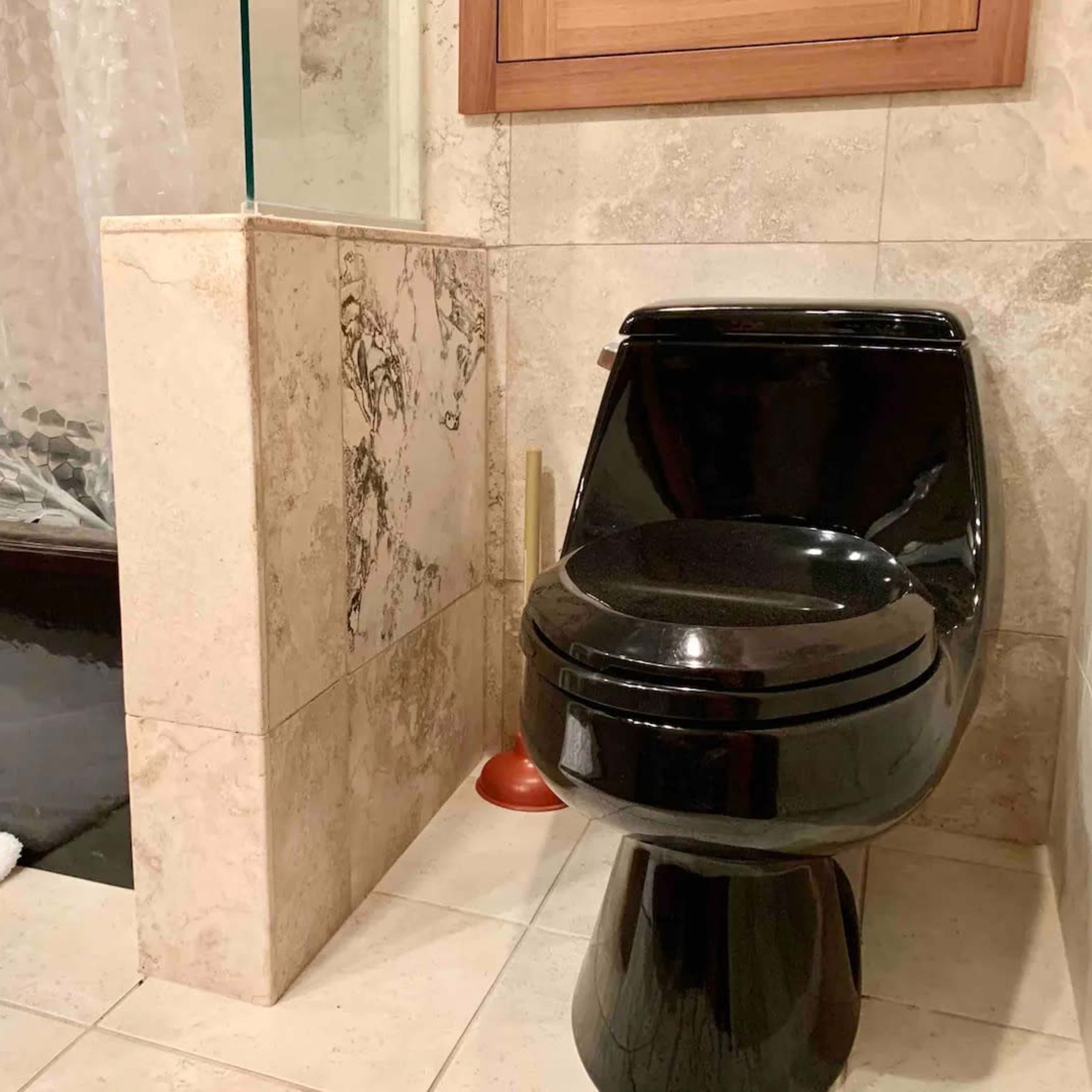 A black toilet positioned next to a shower area with a clear glass panel and a bathtub in a tiled bathroom.