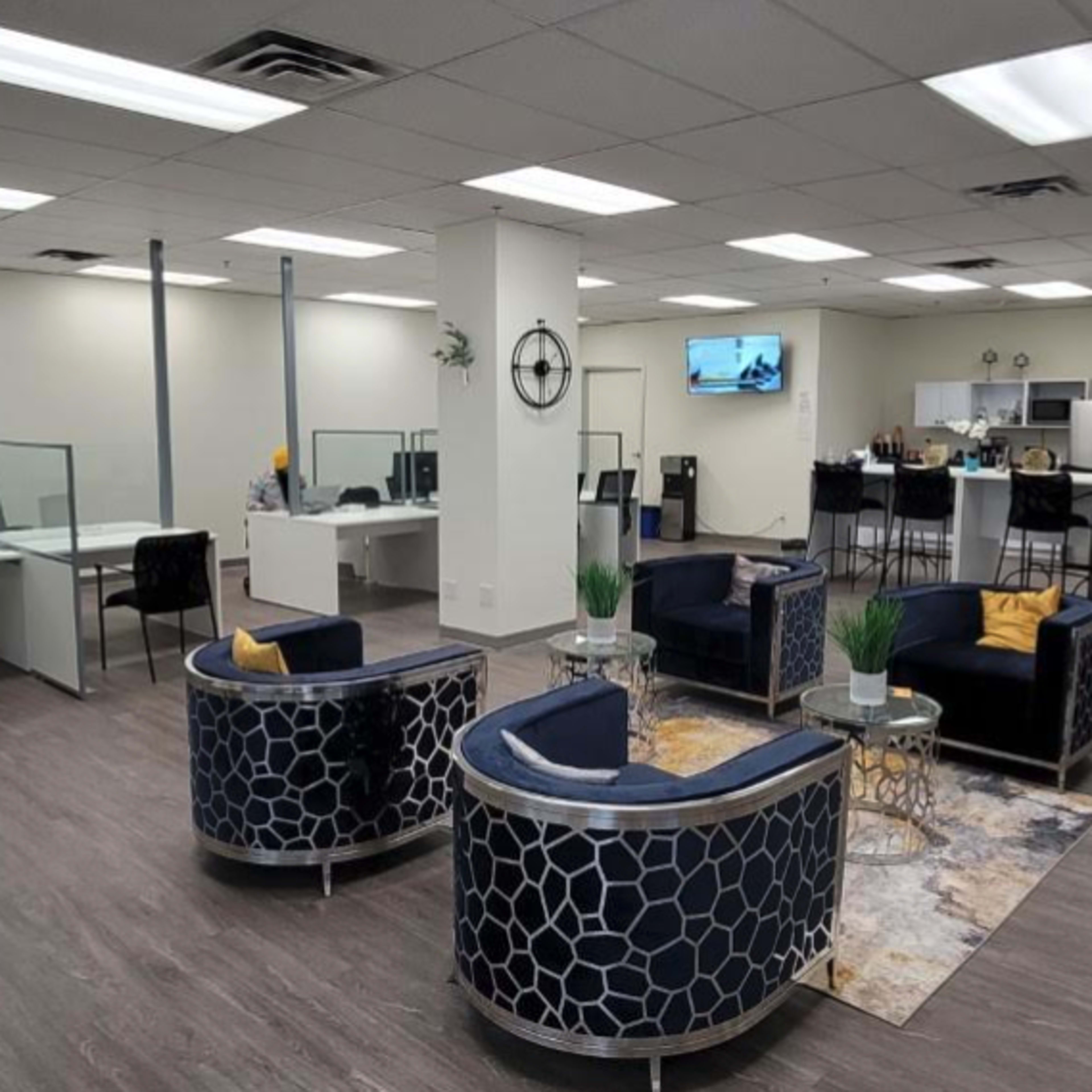 A modern office space with several workstations, a kitchenette, and seating areas arranged around decorative rugs.