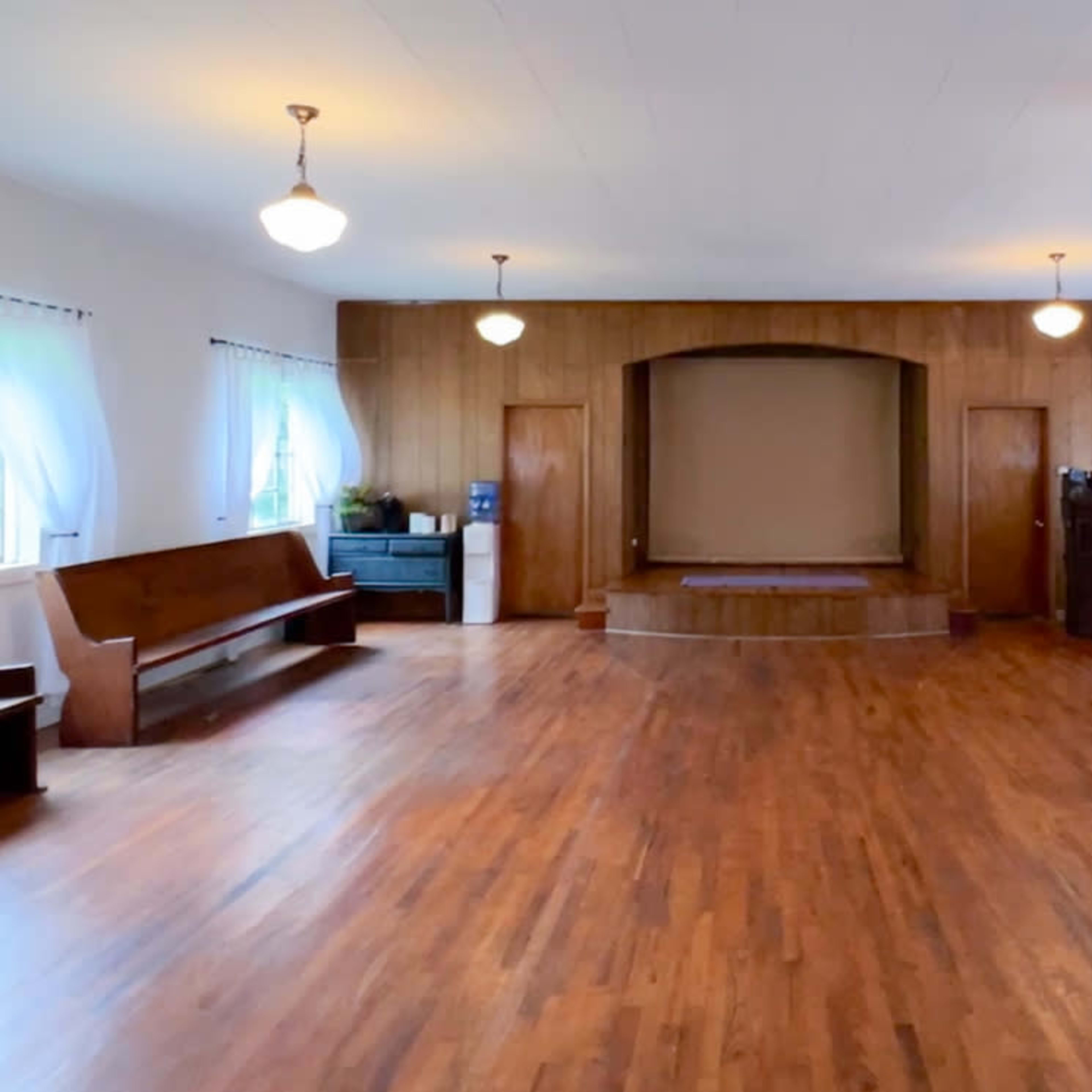 A spacious, empty wooden-floored room with a stage at the back and benches along the walls.