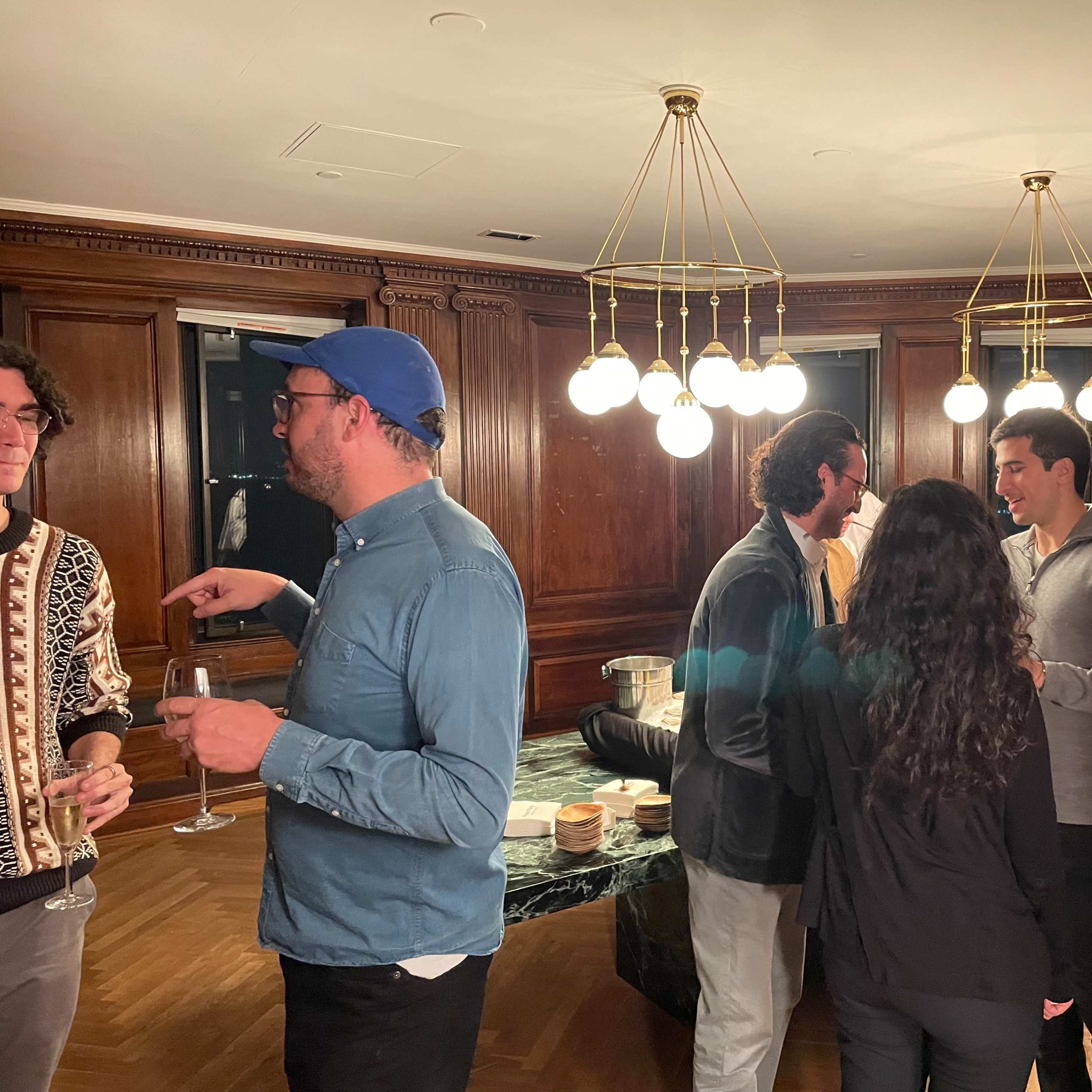 A group of people socialize in a warmly lit room with wooden paneling and modern light fixtures.