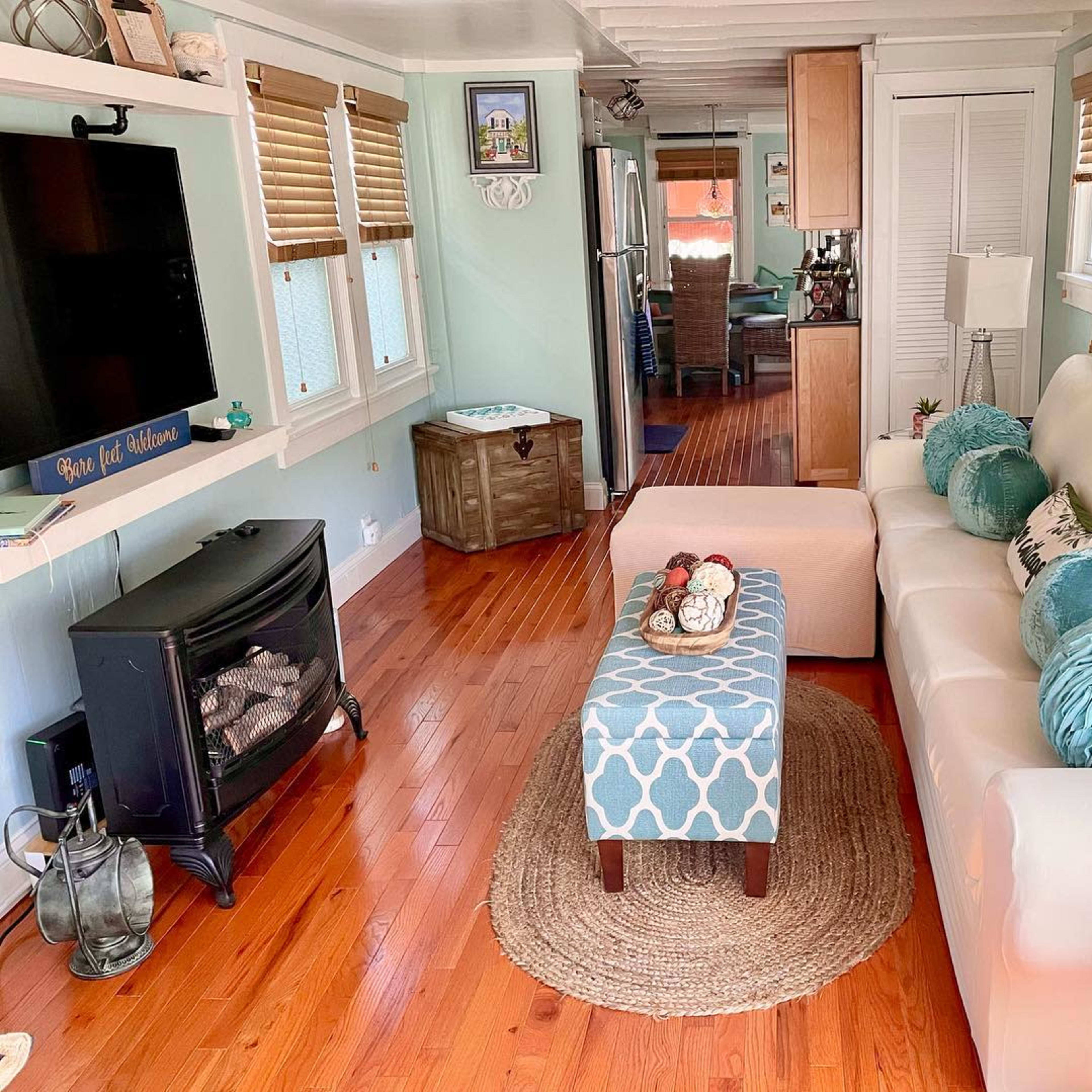 The living room features a white couch, a blue-patterned ottoman, and a fireplace, with wood flooring and green walls.