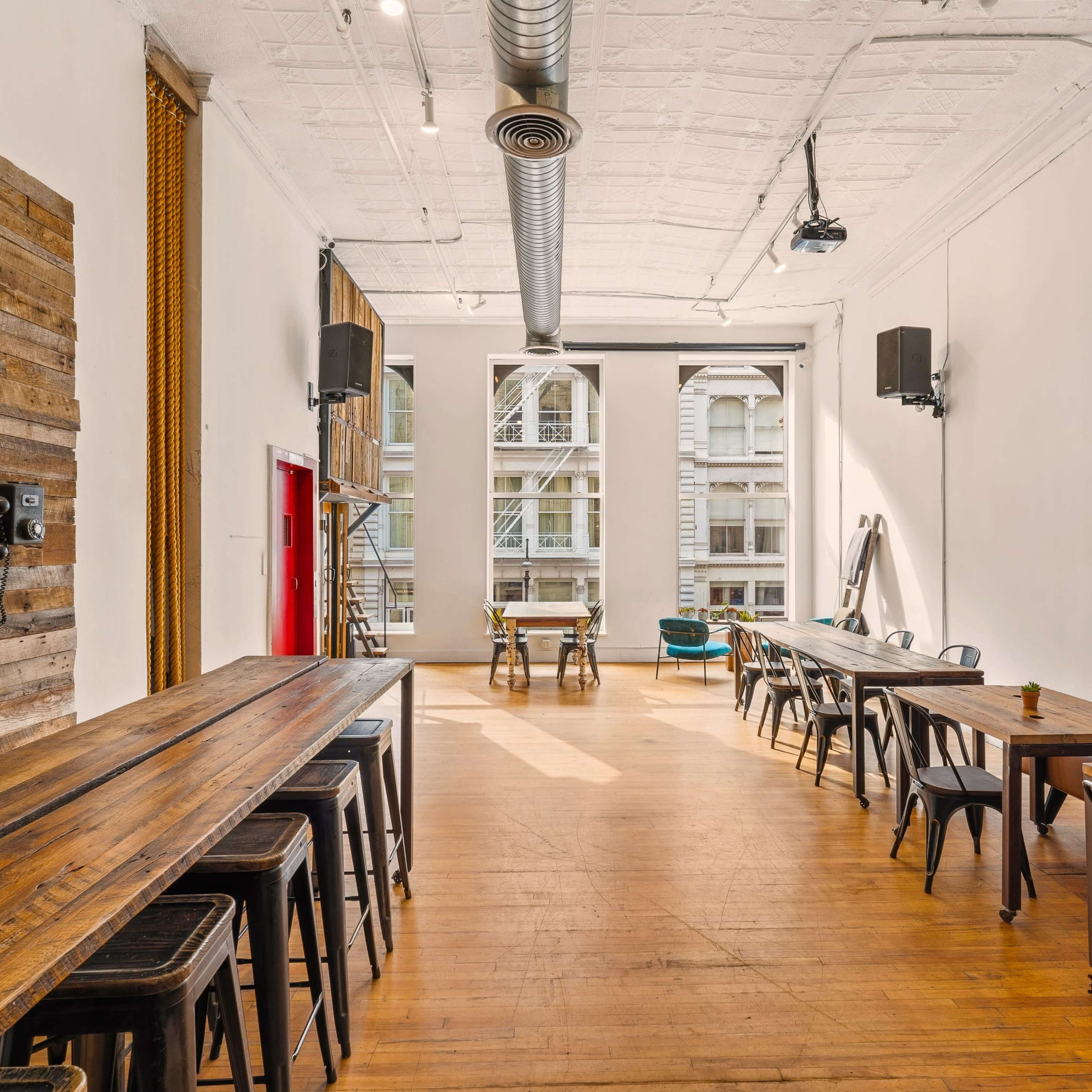 A spacious, minimalist interior of a restaurant or café featuring wooden tables, metal chairs, and a large window with natural light.