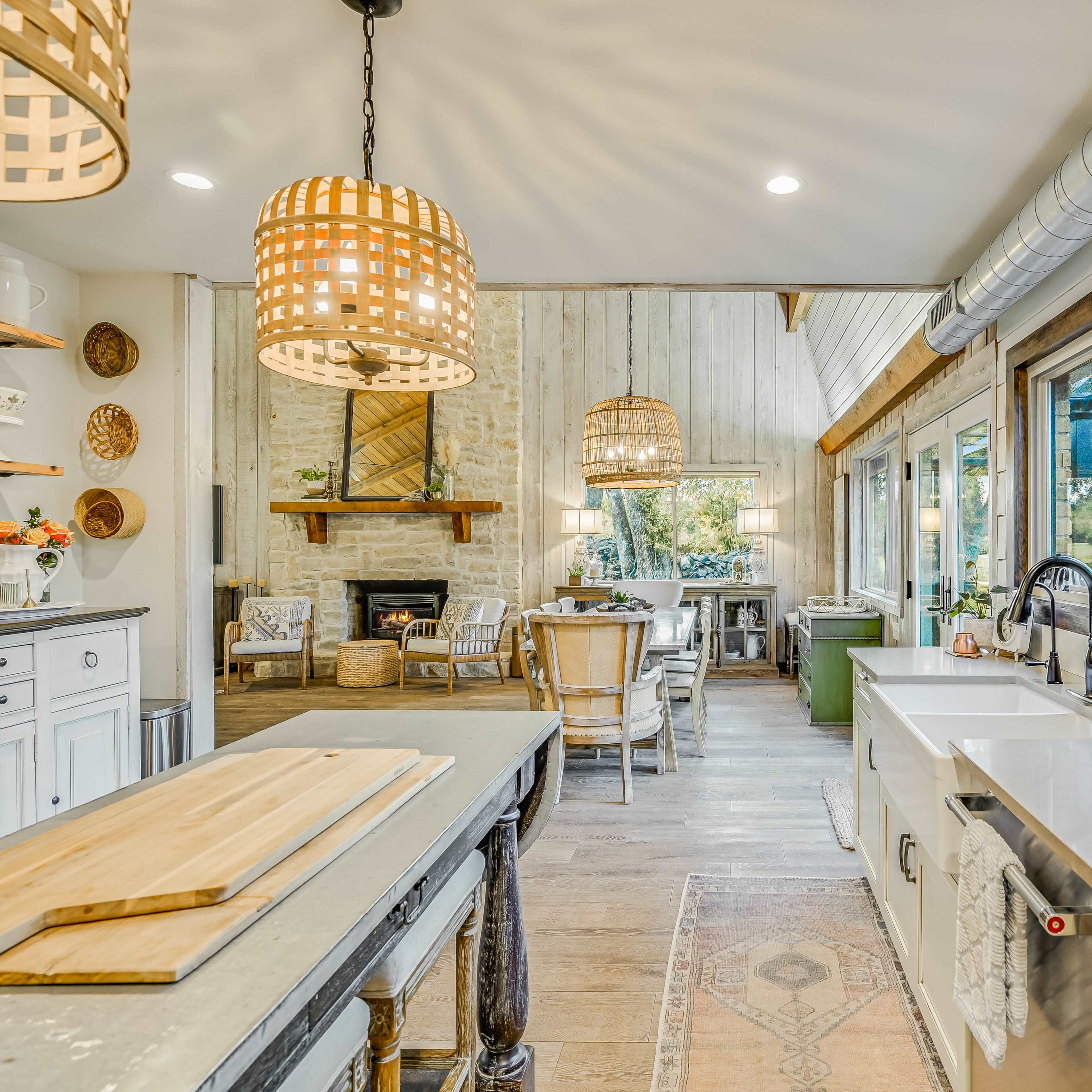 A modern kitchen with an island, pendant lights, and a view of a dining area featuring a fireplace and large windows.