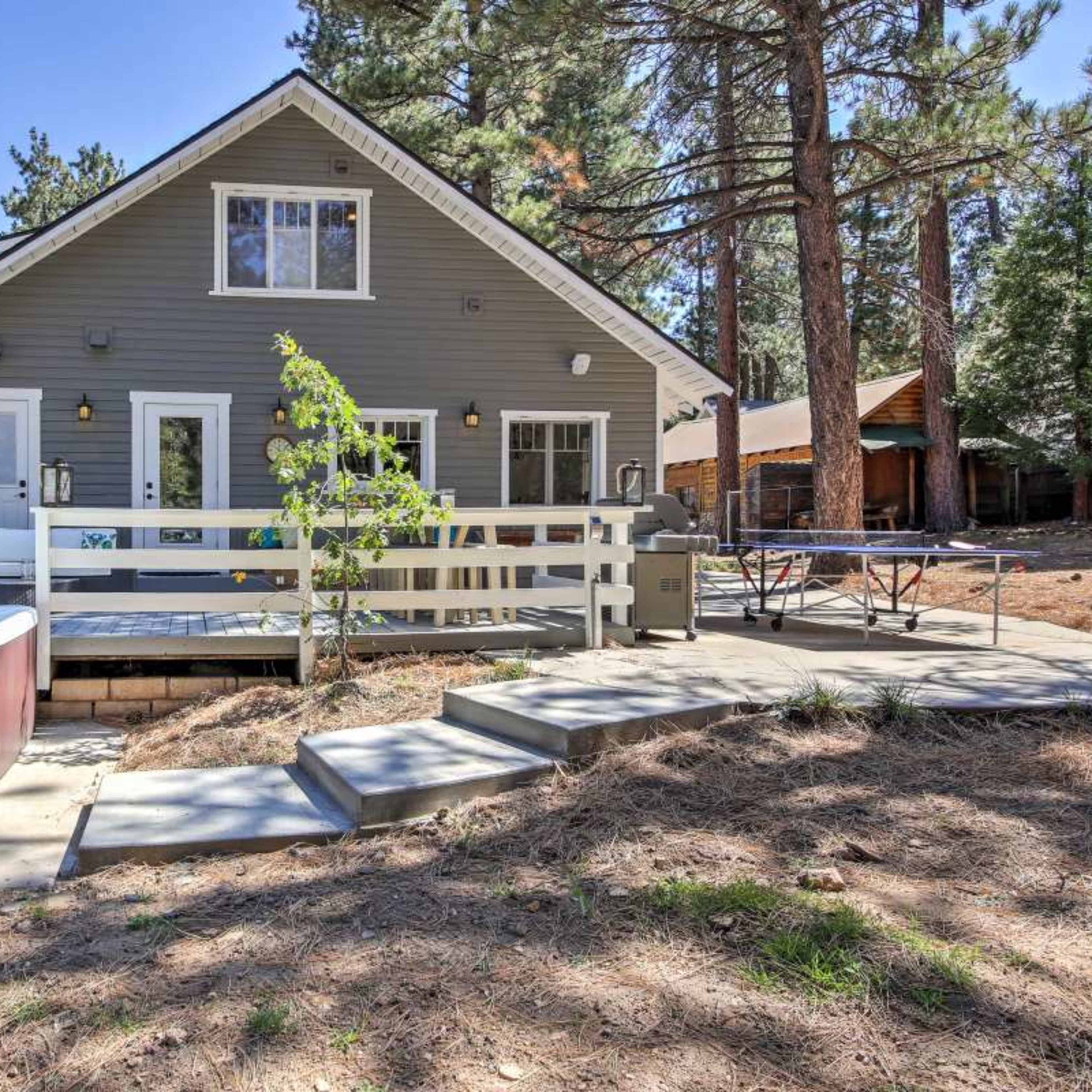 A house with a wooden deck, hot tub, and a small yard surrounded by trees.