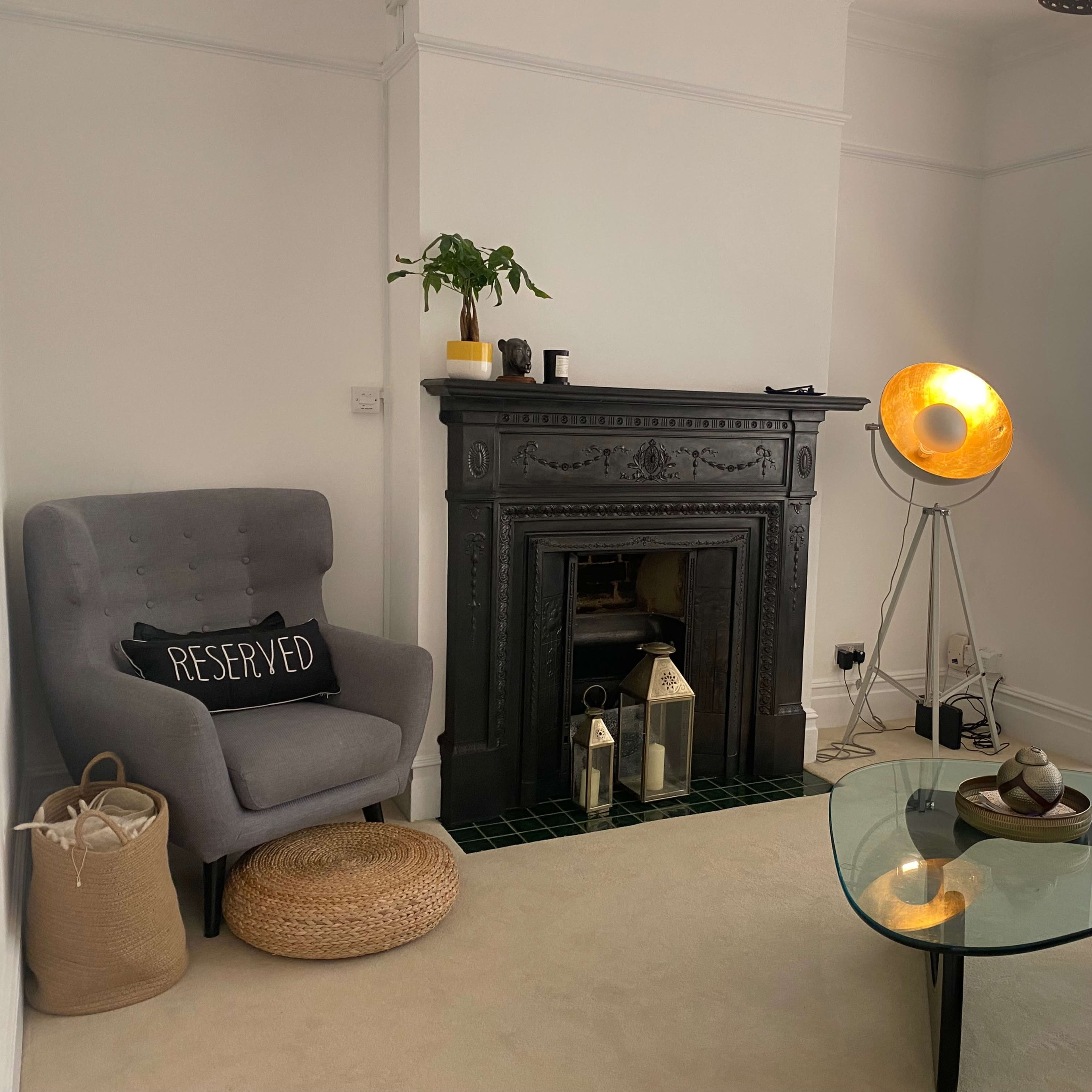 A living room with a gray upholstered chair, a decorative fireplace, a floor lamp, and a glass coffee table.