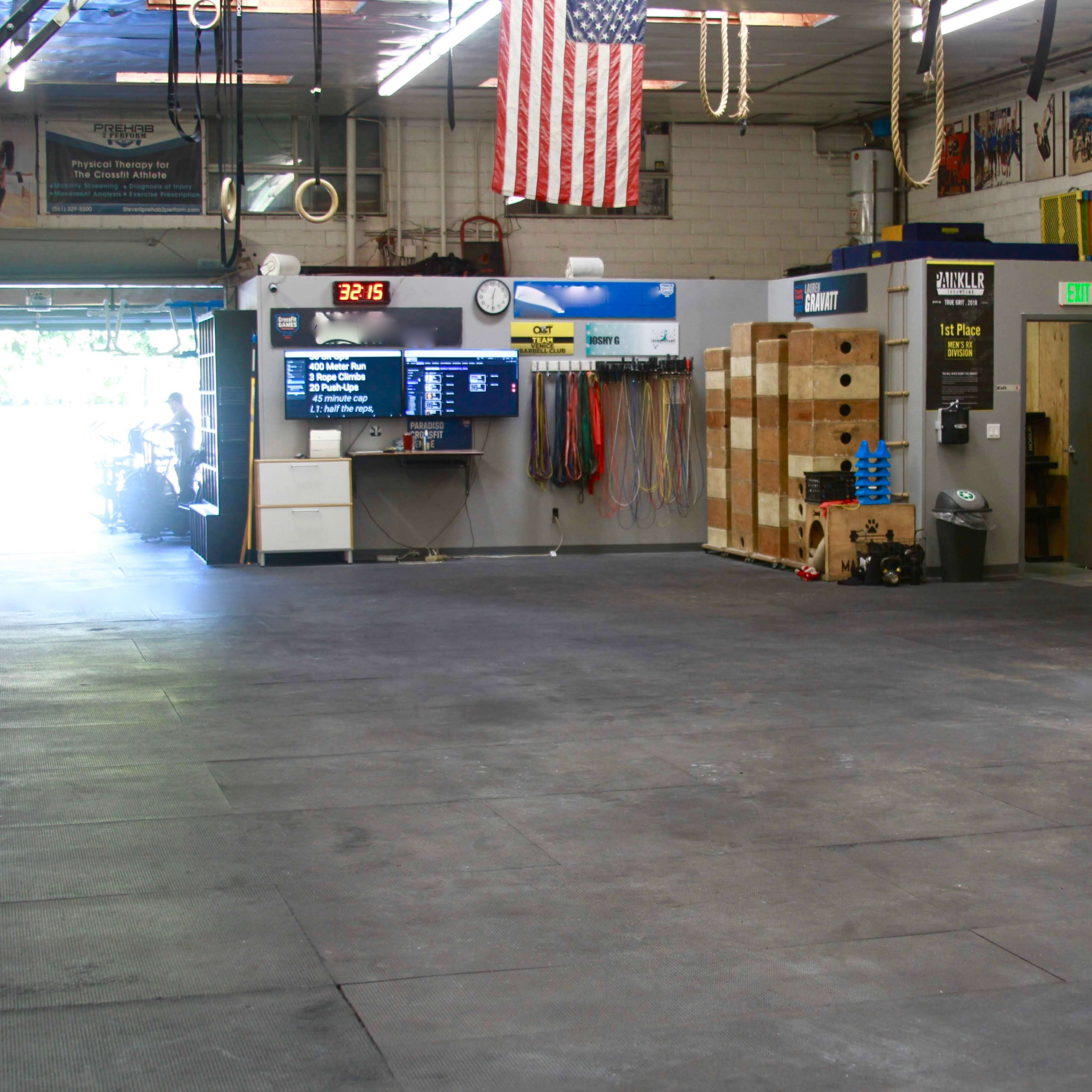 A spacious indoor gym with rubber flooring, exercise equipment, and a large display monitor on the wall.