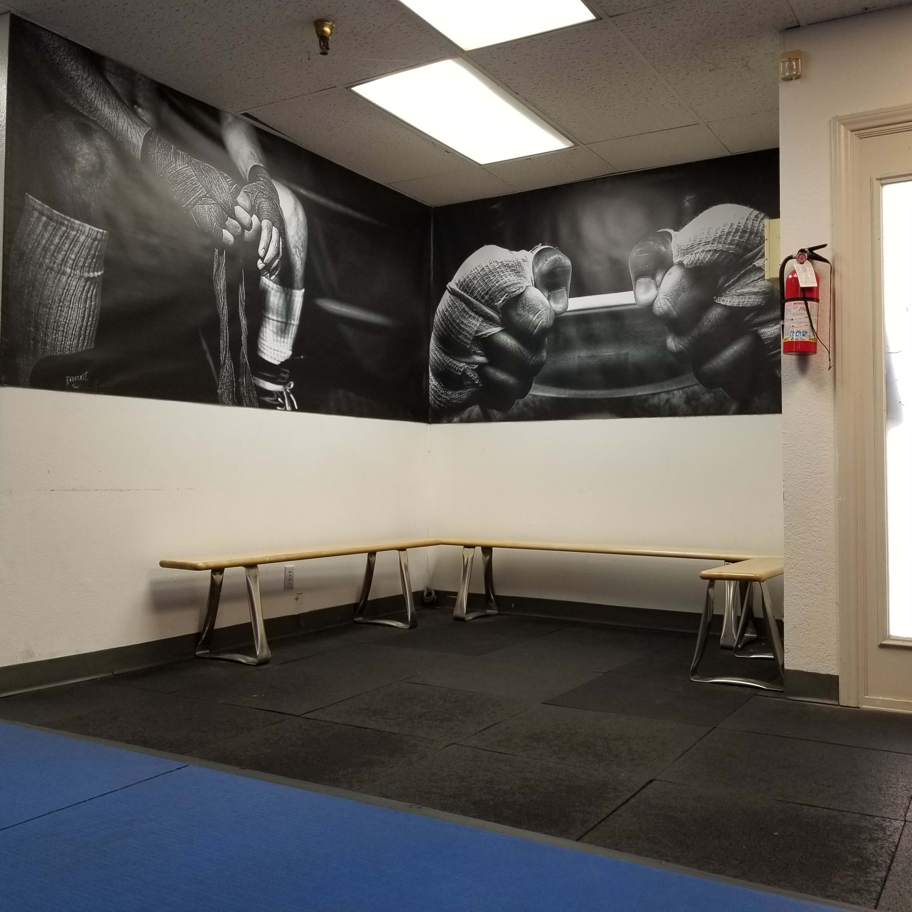 A training room with a large black and white mural of gloved hands preparing equipment, alongside a series of long benches against the walls.
