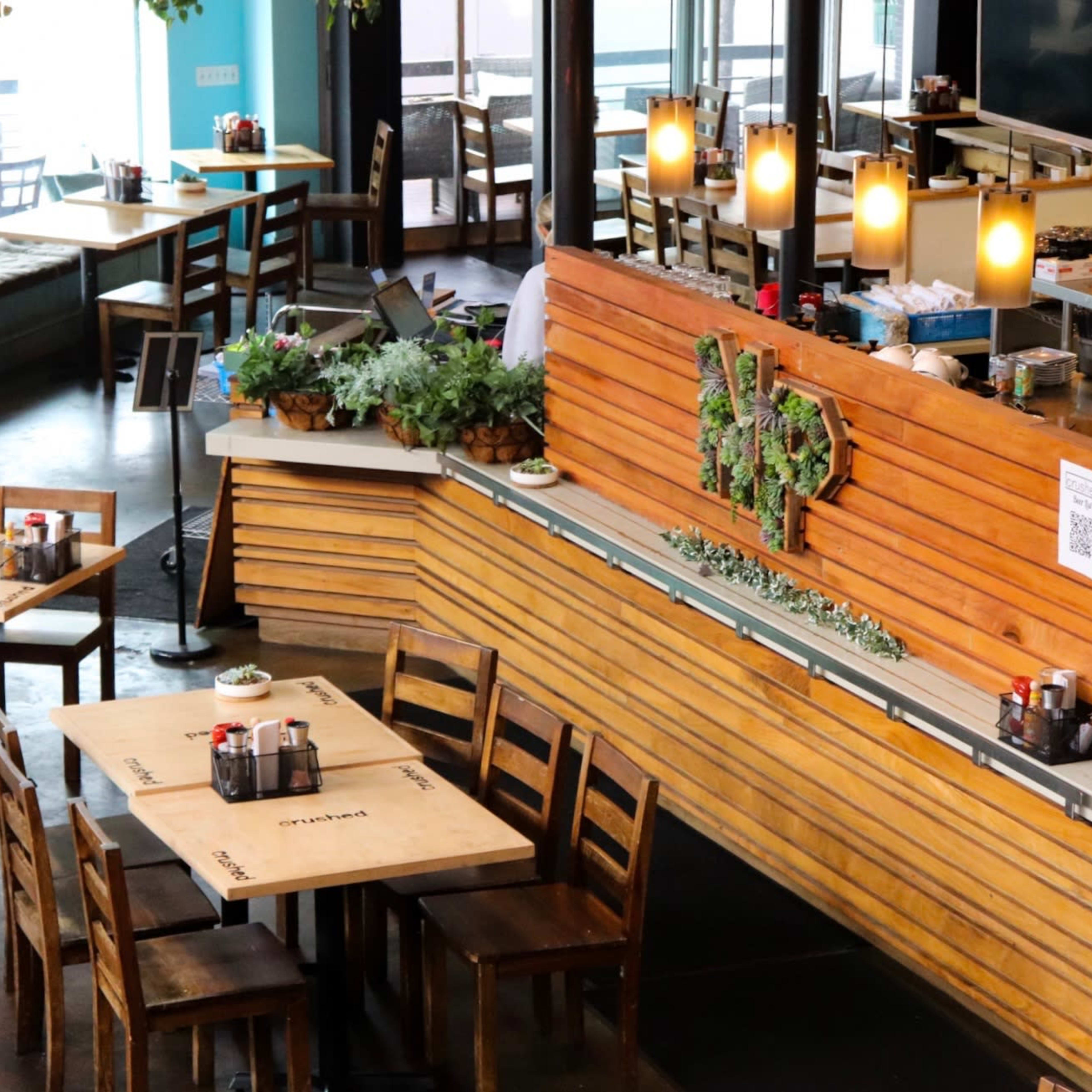 A spacious restaurant interior features wooden tables and chairs, with a counter displaying plants and QR codes.