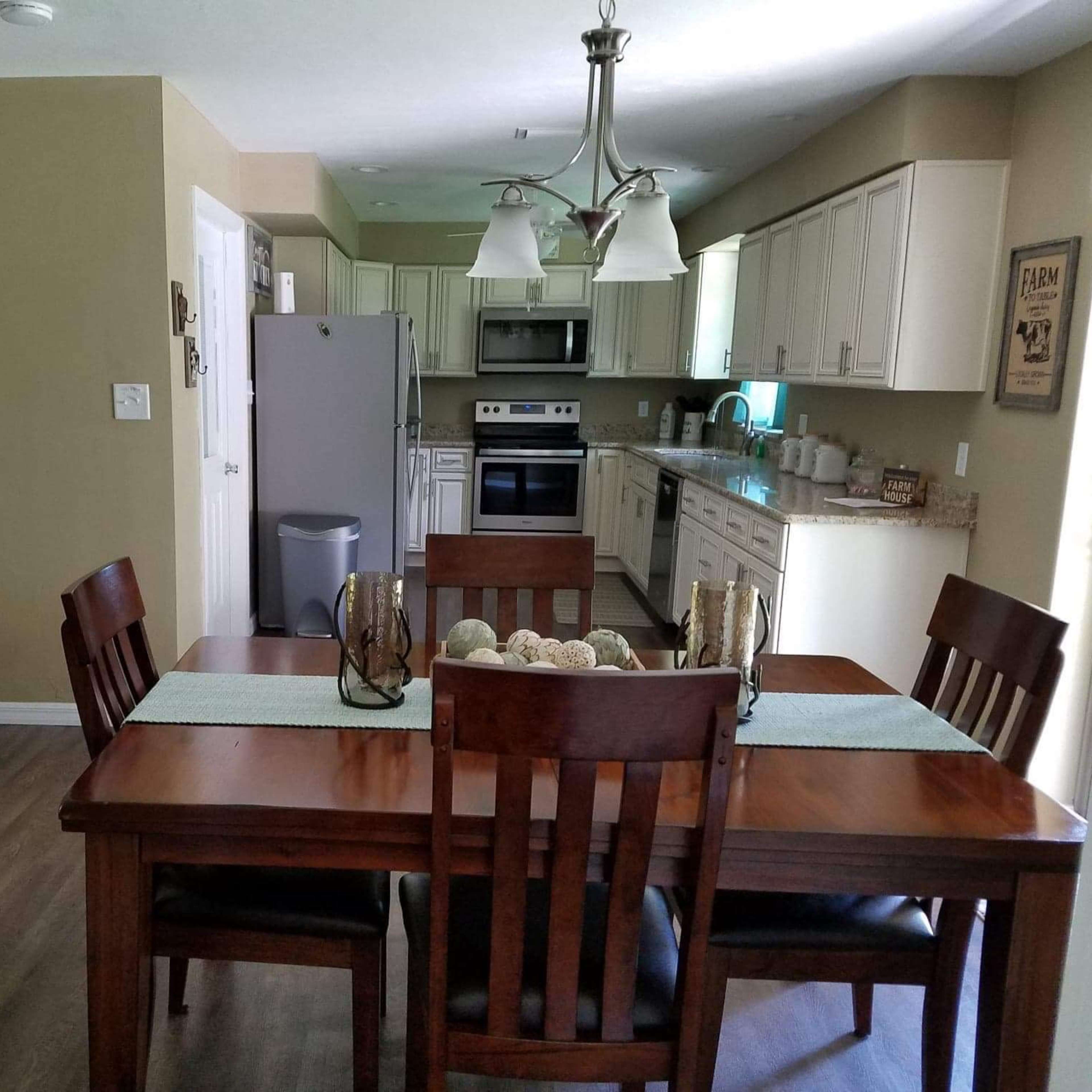 A kitchen and dining area featuring a wooden dining table with chairs, a beige wall, and modern kitchen appliances.