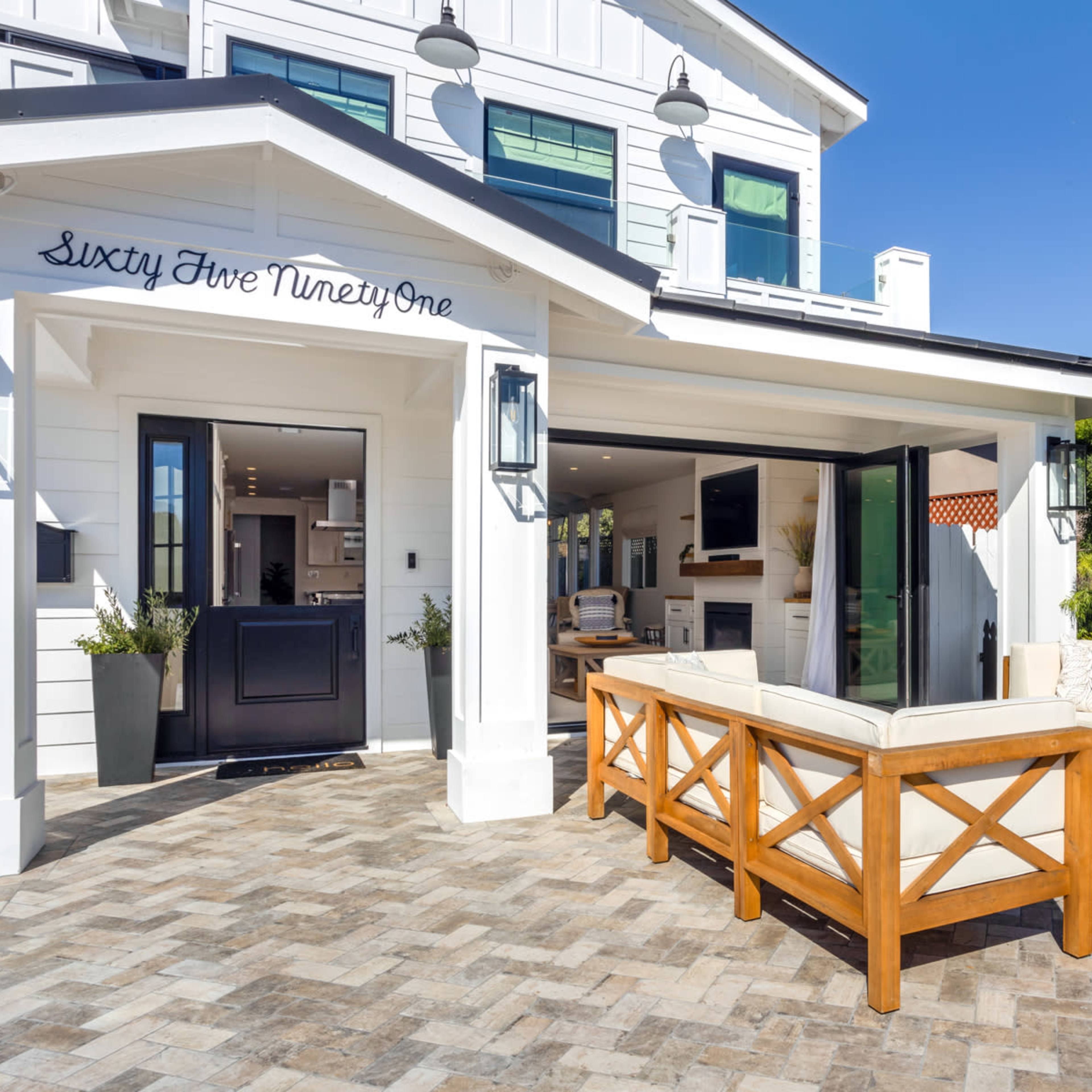 A modern outdoor seating area features a light-colored sectional couch and wooden accents in front of a contemporary home.
