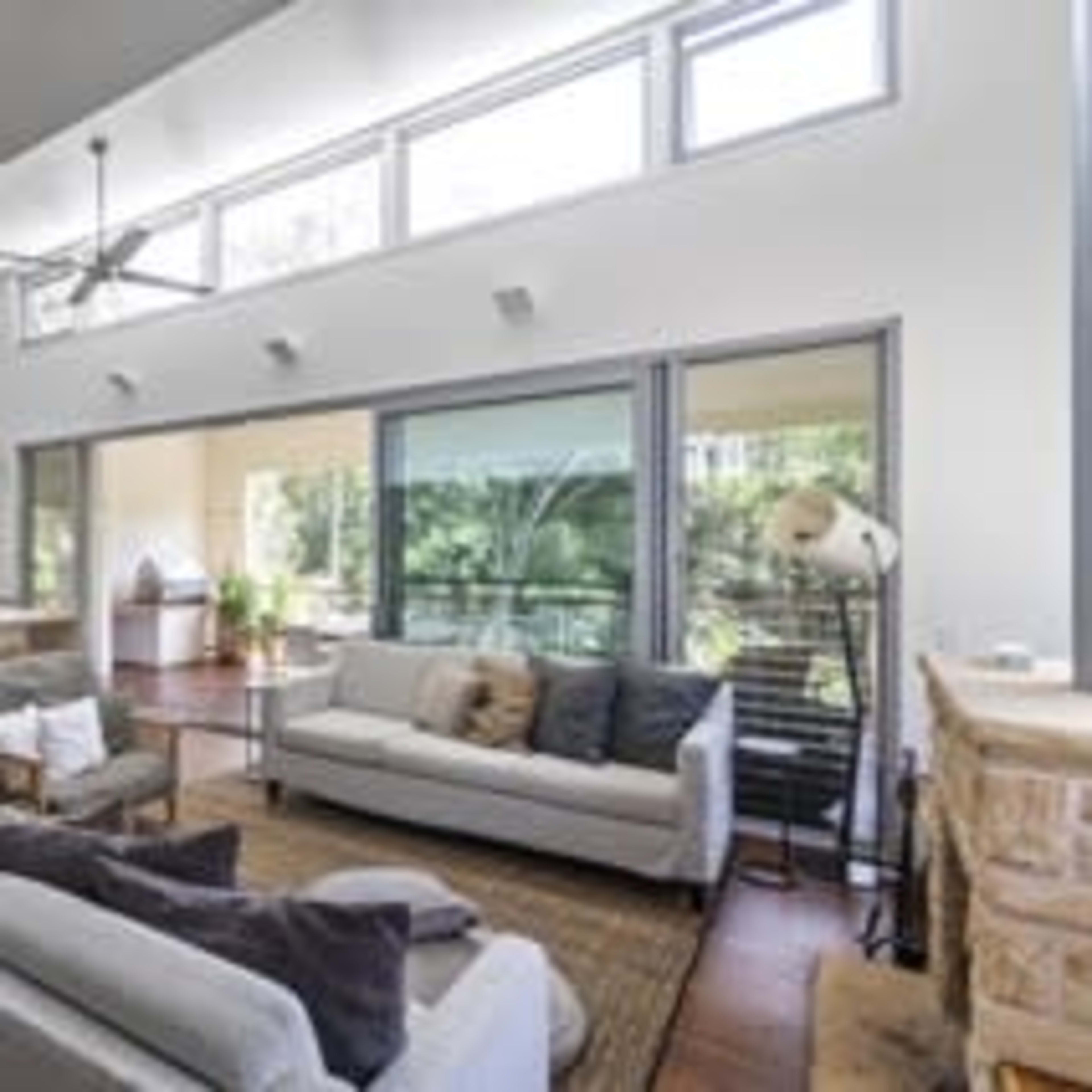 A bright, open-plan living room with two sofas, a coffee table, and large windows overlooking a green outdoor area.