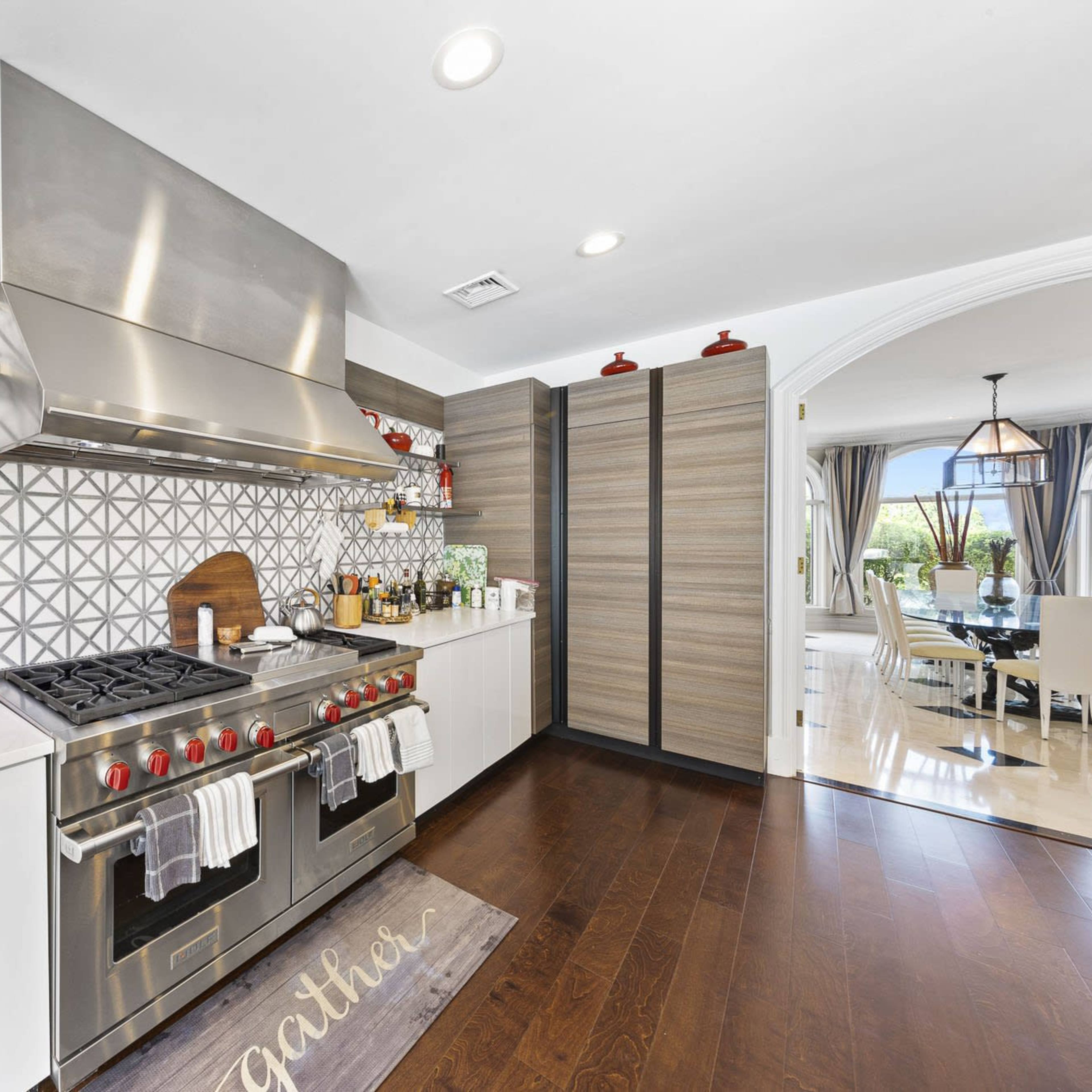 A modern kitchen featuring a stainless steel gas stove, white cabinetry, geometric tile backsplash, and open shelving with decorative items.