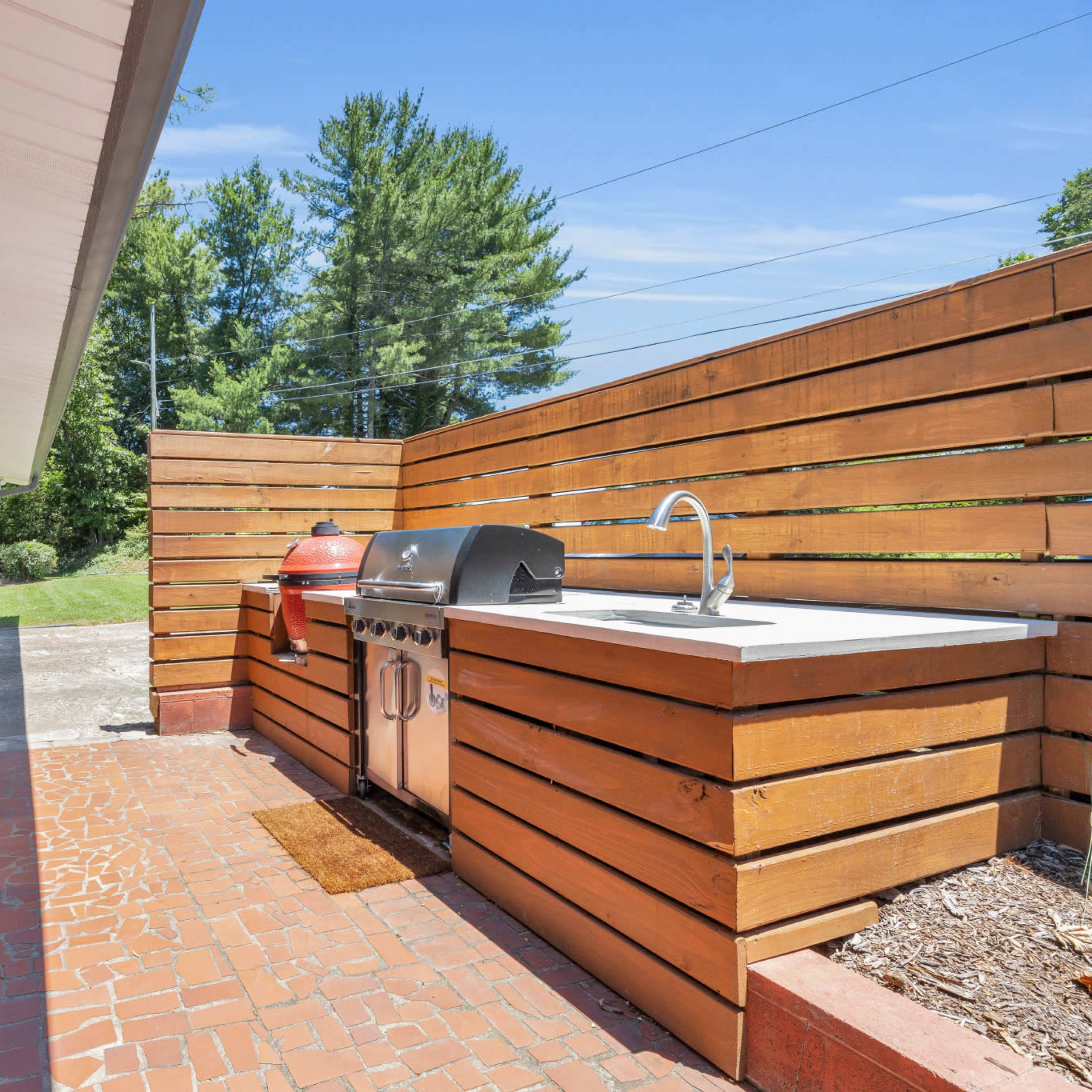 An outdoor kitchen area with a grill, sink, and bar seating surrounded by wooden fencing.