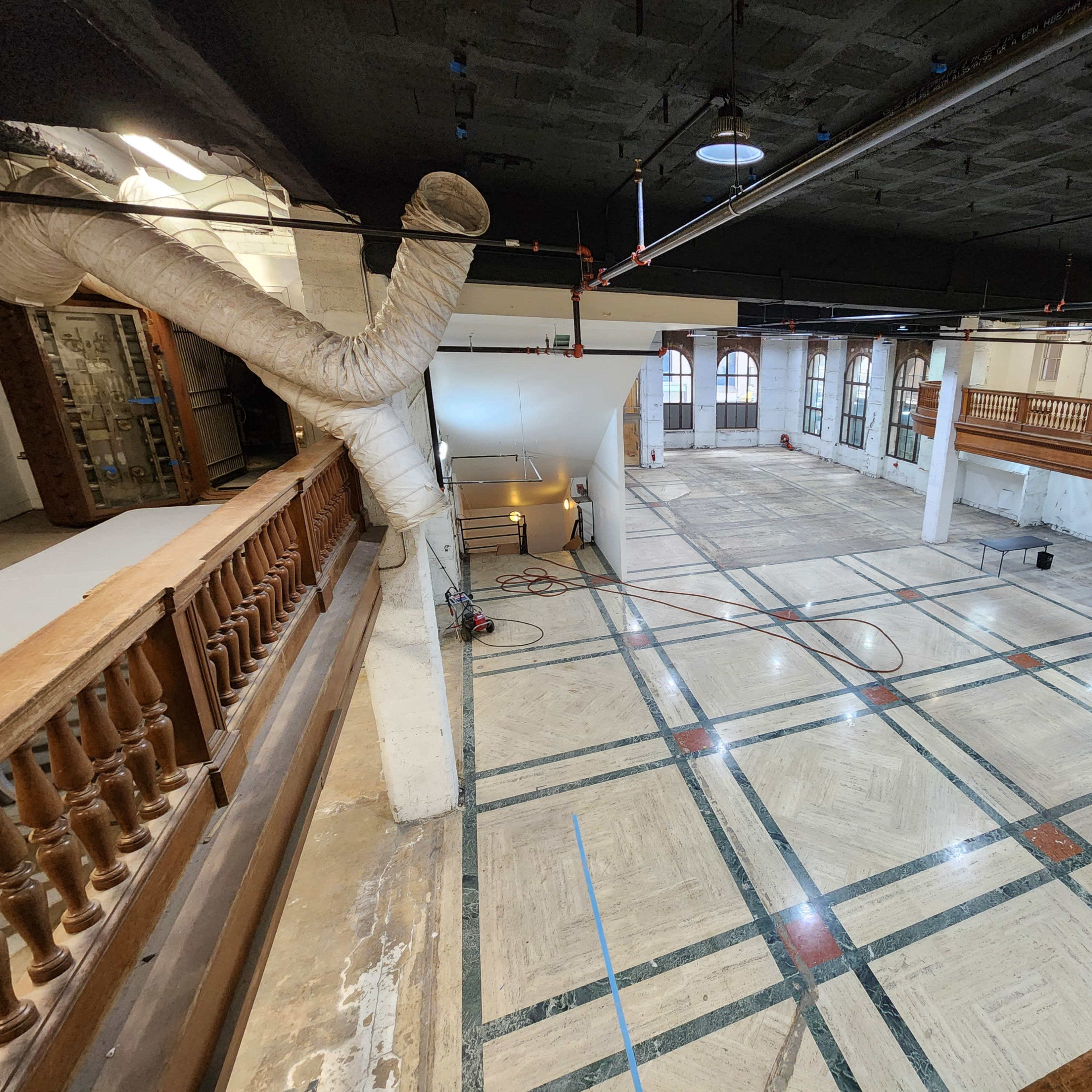 An expansive, empty room with a patterned floor and large windows, featuring a balcony overlooking the space.