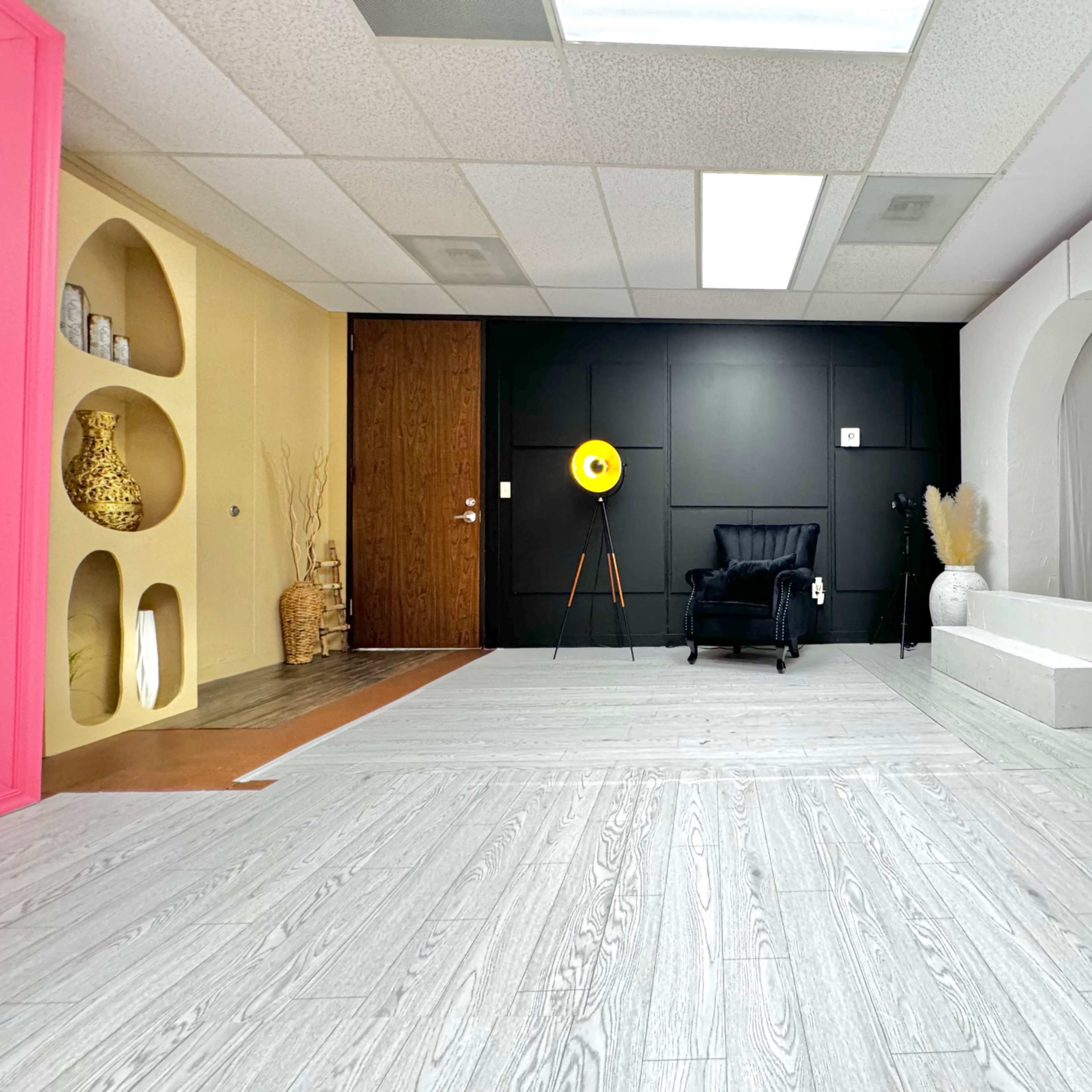 A bright, modern interior space with white flooring, a black accent wall, a large mustard-colored round light fixture, and decorative vases.