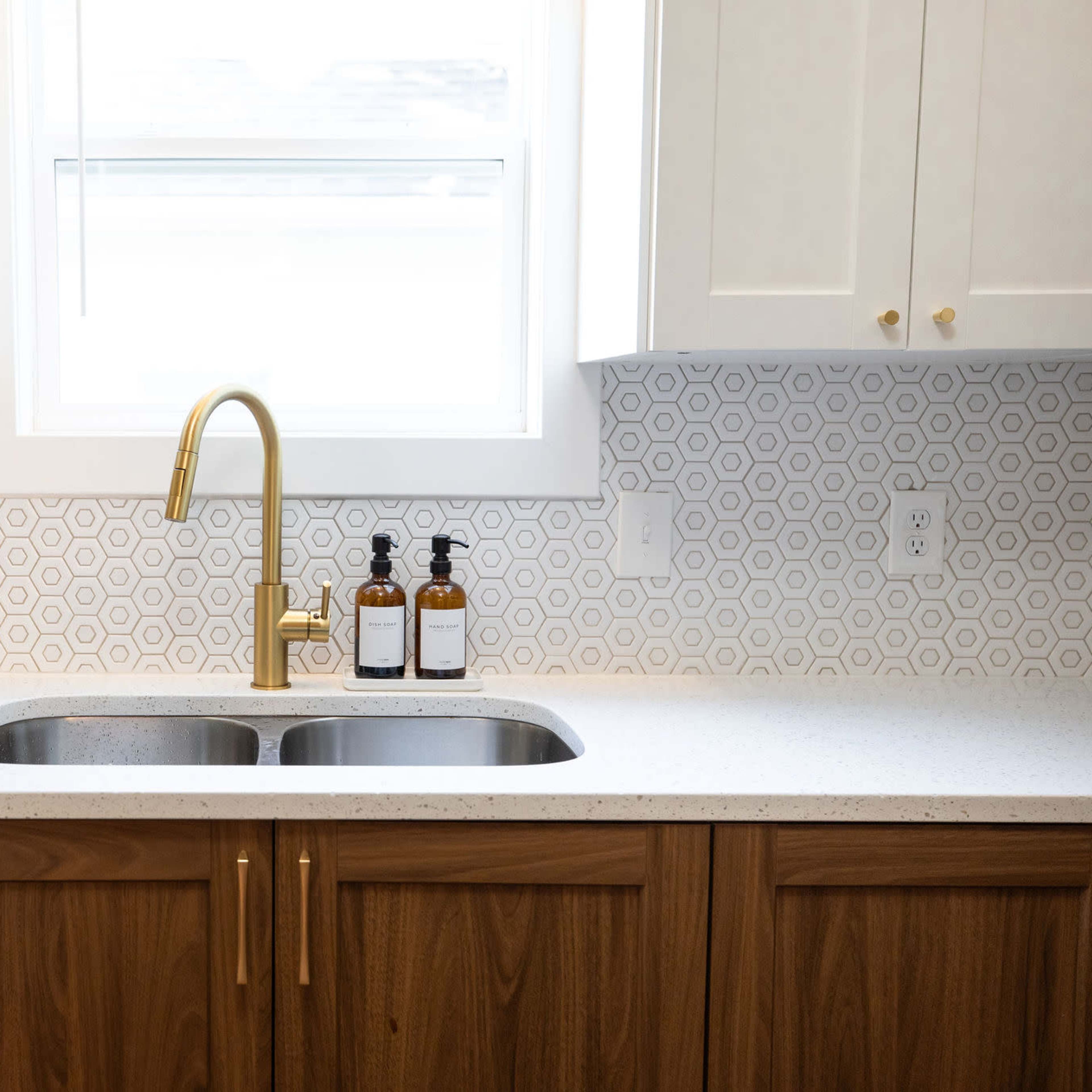 A modern kitchen features a double sink with a gold faucet, surrounded by white cabinets and a hexagonal patterned backsplash.