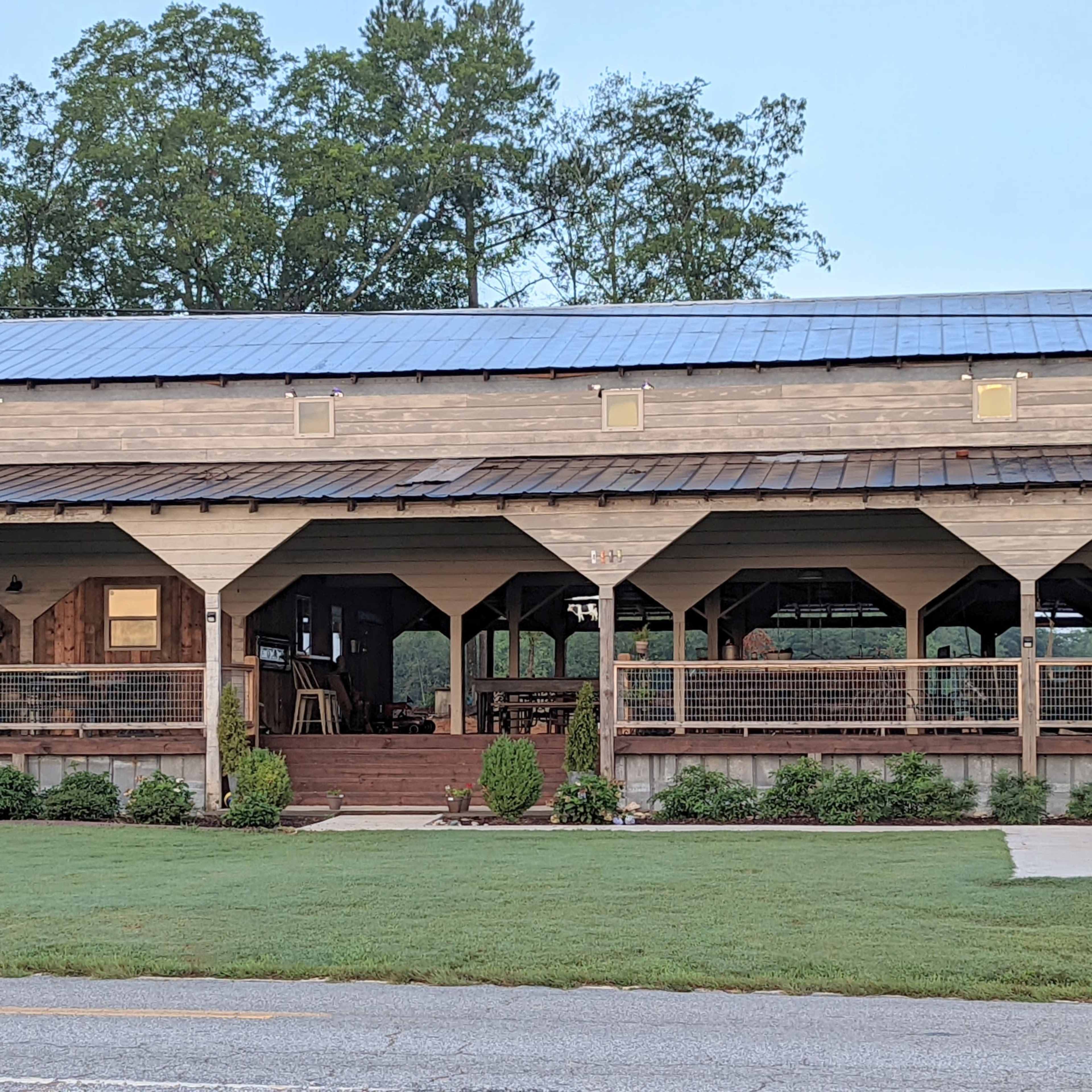 A two-story wooden building with a covered porch and large windows, set against a backdrop of trees and grass.