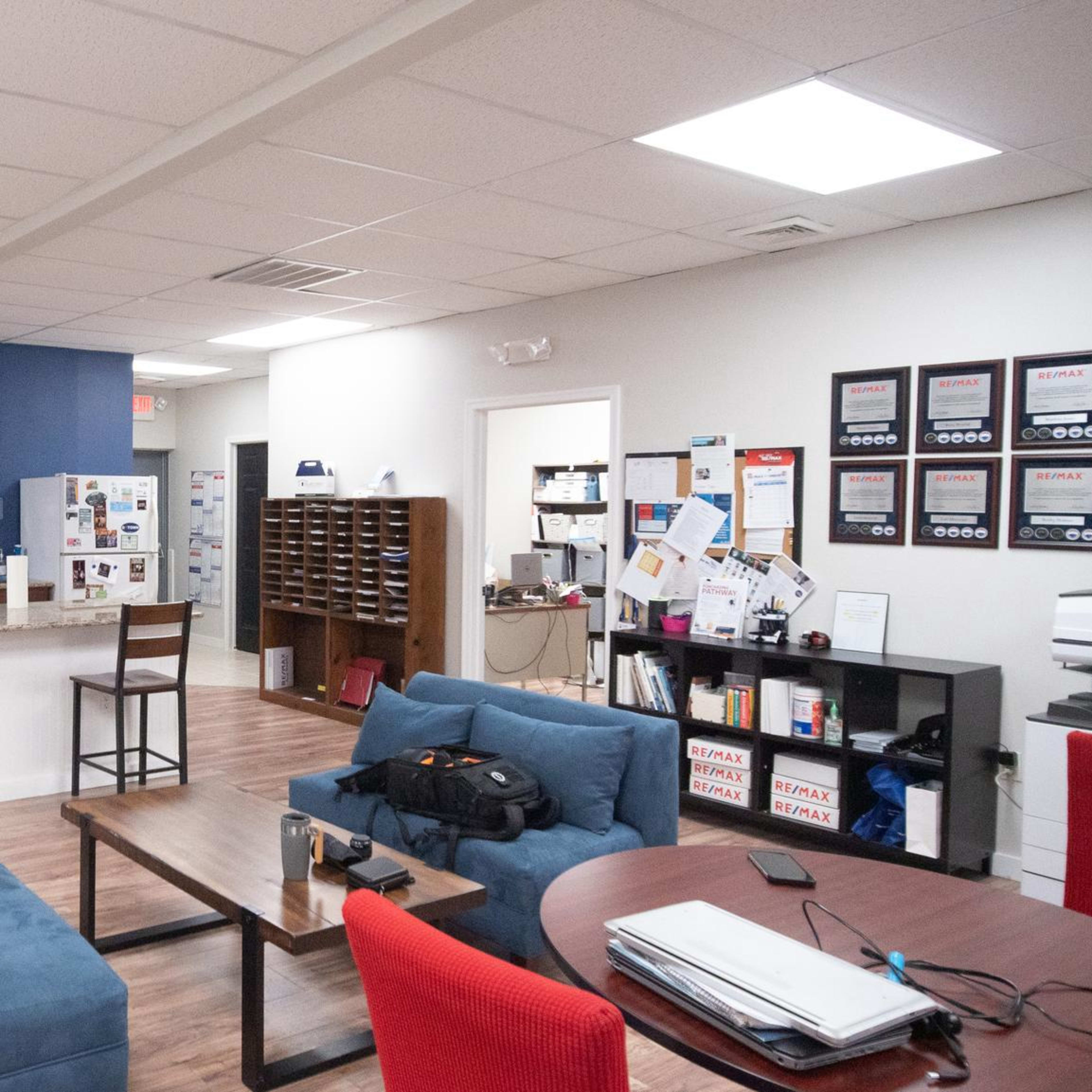 A modern break room featuring a lounge area with blue sofas, a kitchenette with bar stools, and a wall of mail slots.