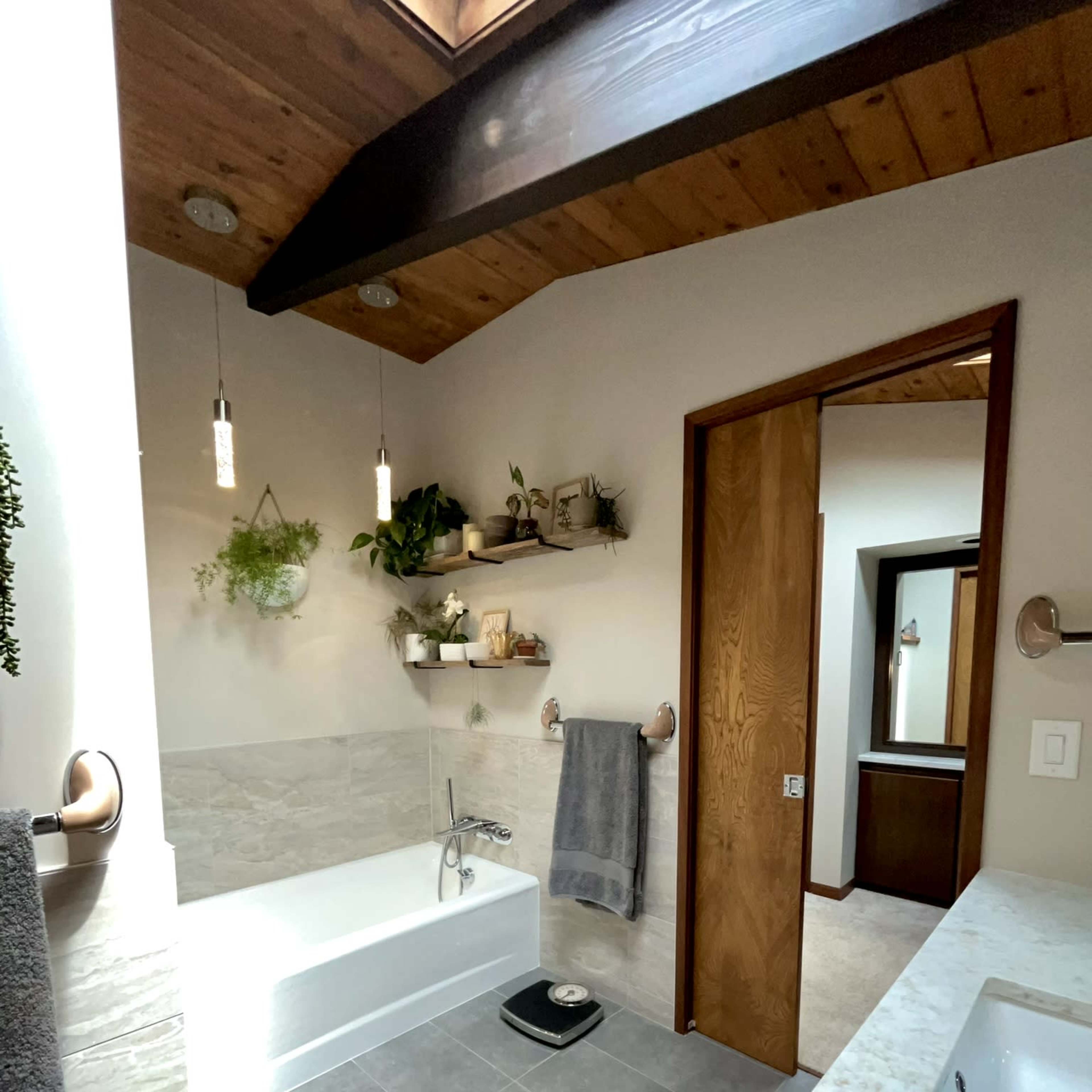 A well-lit bathroom features a bathtub, a shower area, a sink with marble countertops, and wooden accents.