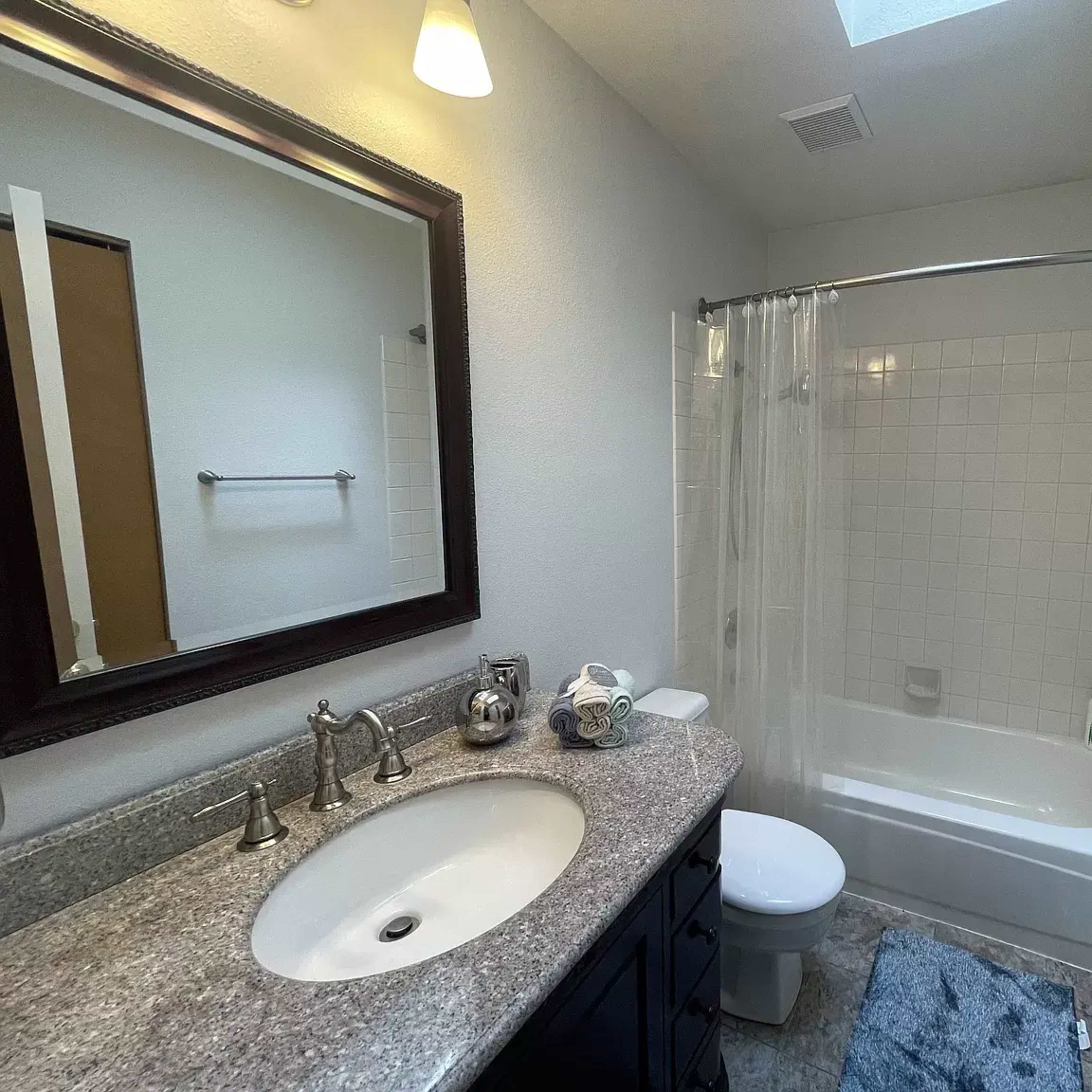A bathroom featuring a bathtub with a shower curtain, a vanity with a sink, and a large mirror above it.