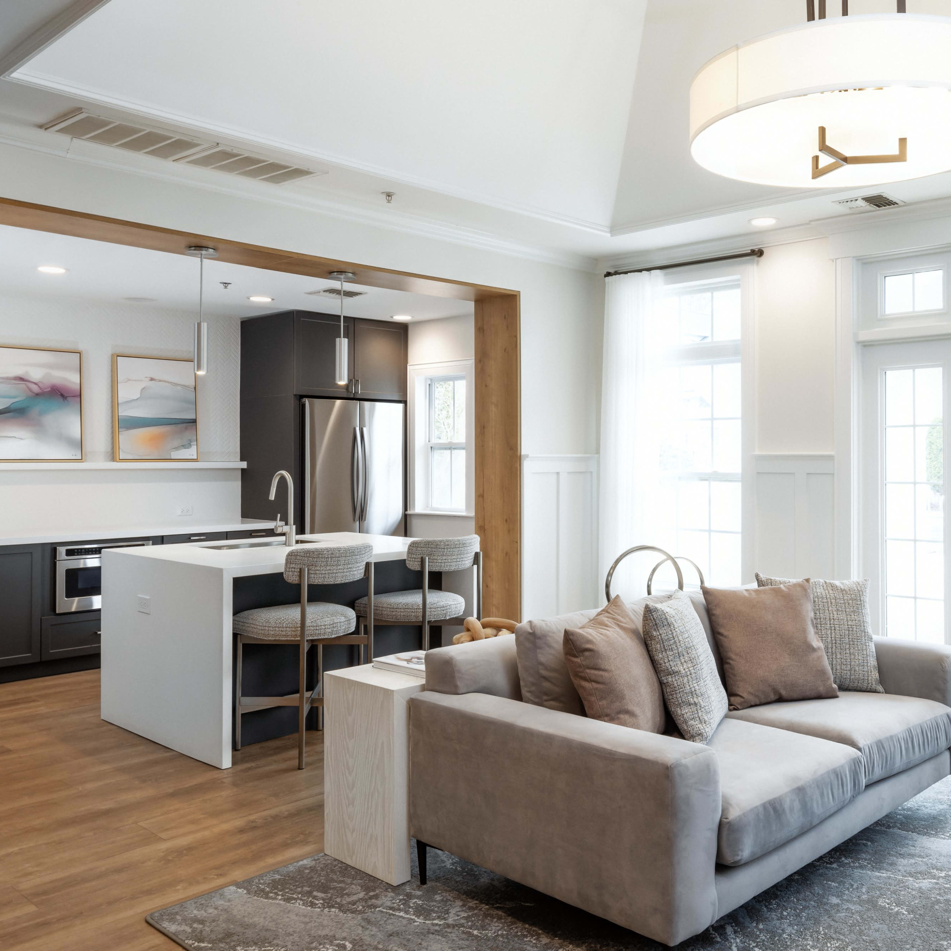 A modern living room with a gray sofa, a small round table, and an adjoining kitchen area featuring a sleek design and stainless steel appliances.