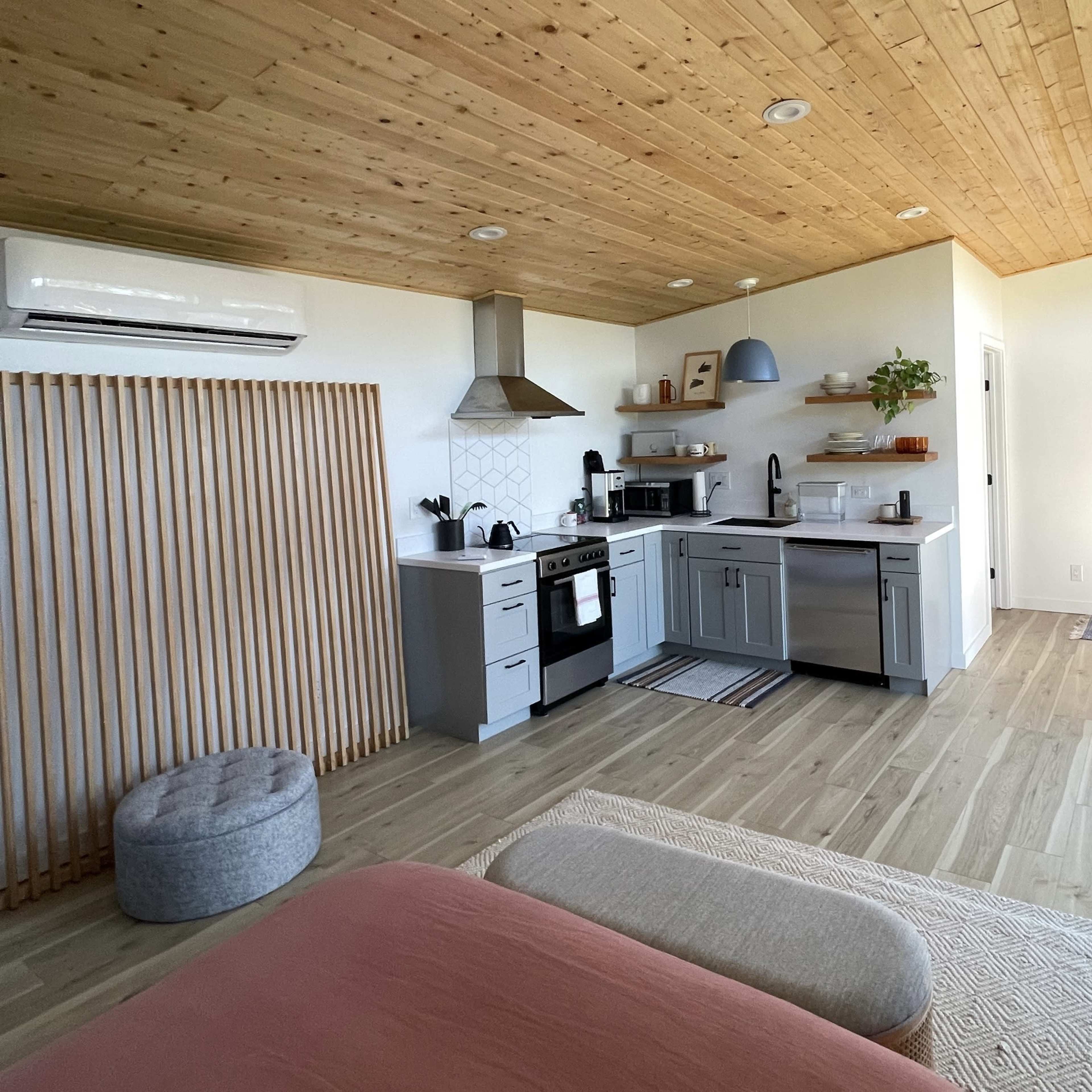 A modern kitchen area featuring gray cabinets, a stainless steel stove, and a wooden ceiling in a well-lit open space.