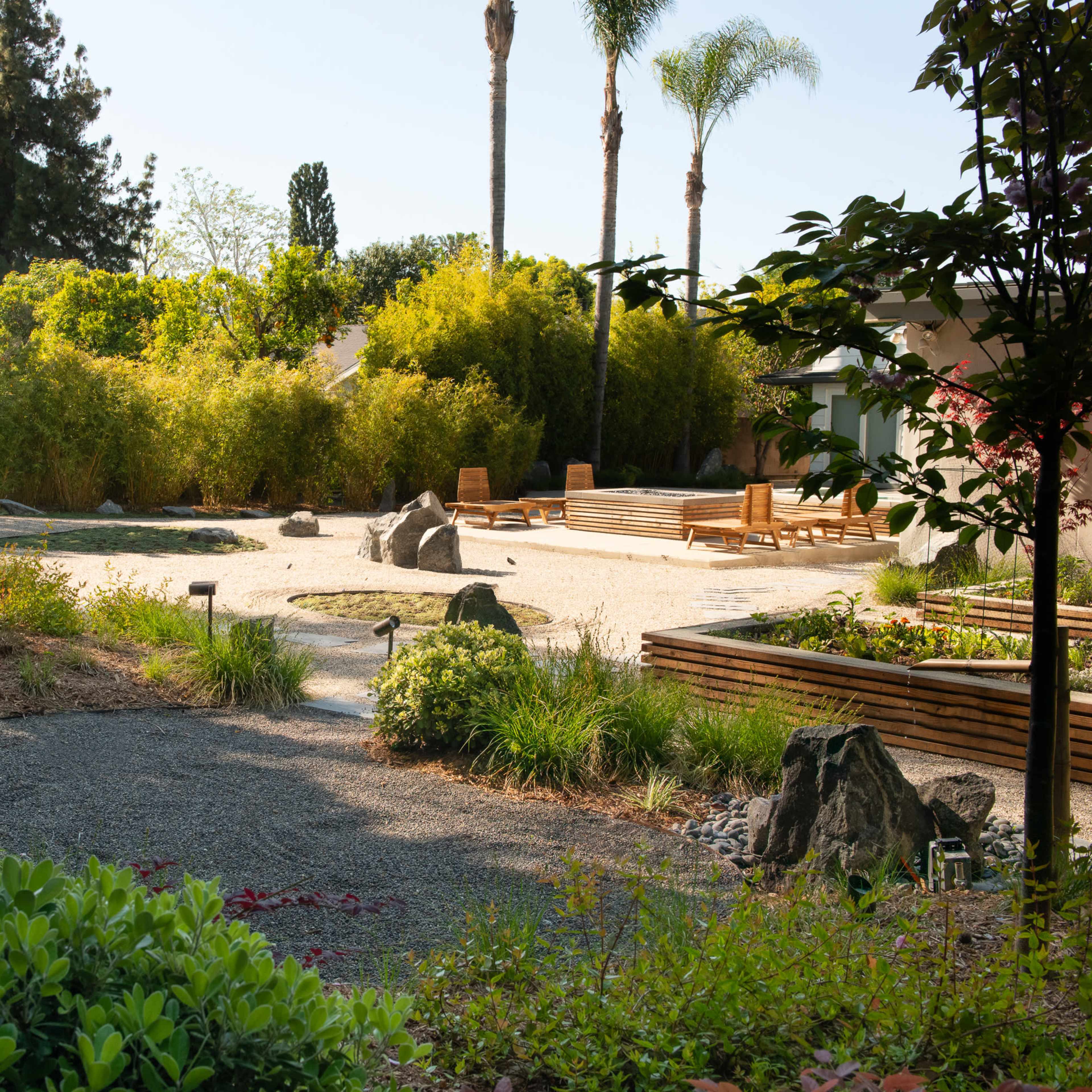 A landscaped garden features gravel paths, rocks, and various plants, with palm trees and bamboo in the background.