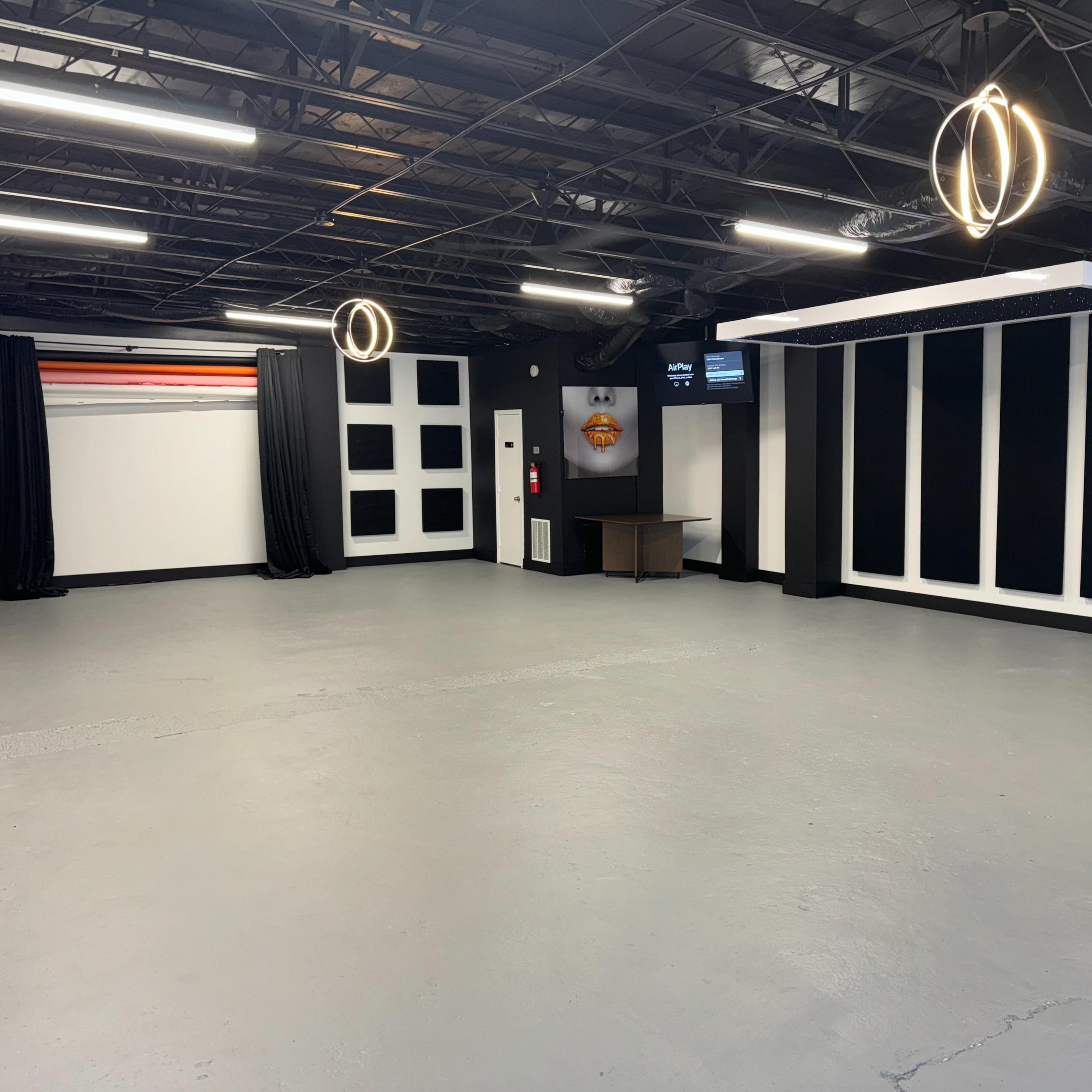 A spacious room with a gray floor, black walls, and two circular light fixtures hanging from the ceiling.